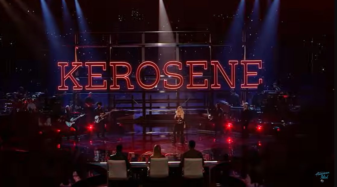 A wide shot shows Miranda Lambert performing with "Kerosene" in red lights behind her as the judges and audience watch on "American Idol" | Source: YouTube/AmericanIdol