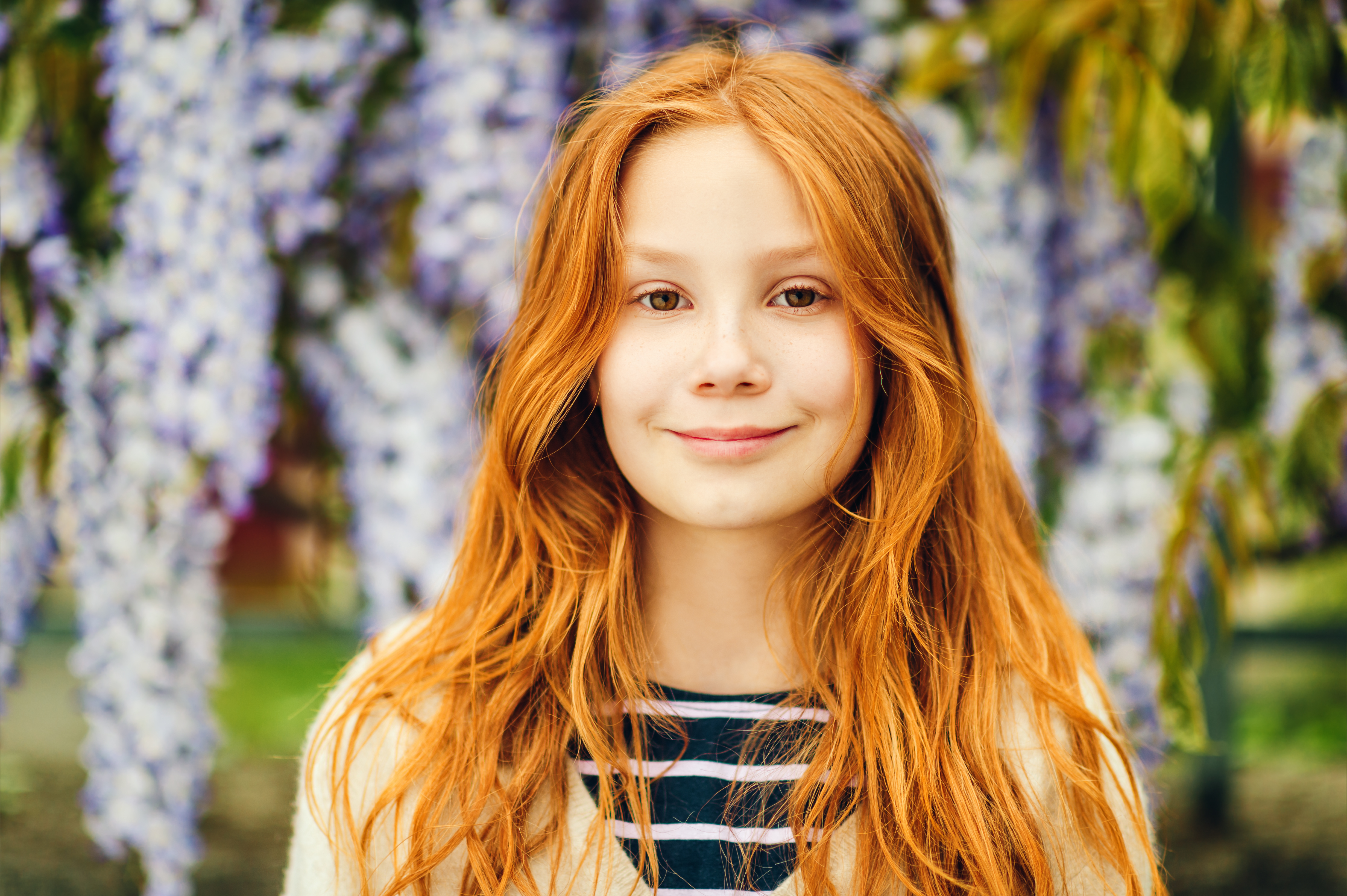 A young girl smiling in front of a wisteria tree | Source: Shutterstock