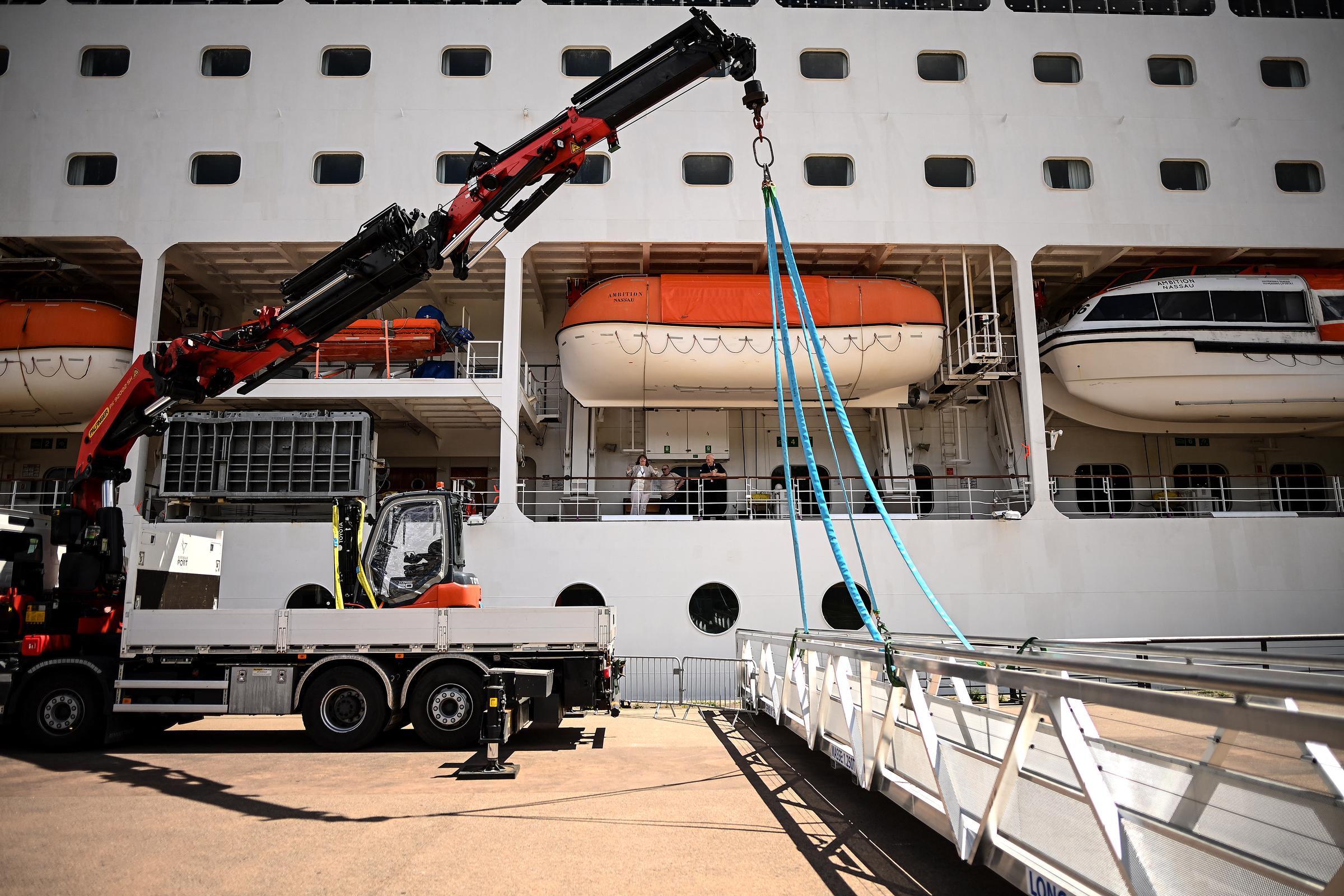 Passengers stand aboard the Bahamas-registered cruise ship Ambition after they were confined following the outbreak of a gastrointestinal illness onboard, at the Bordeaux port in Bordeaux, southwestern France on May 13, 2026. | Source: Getty Images