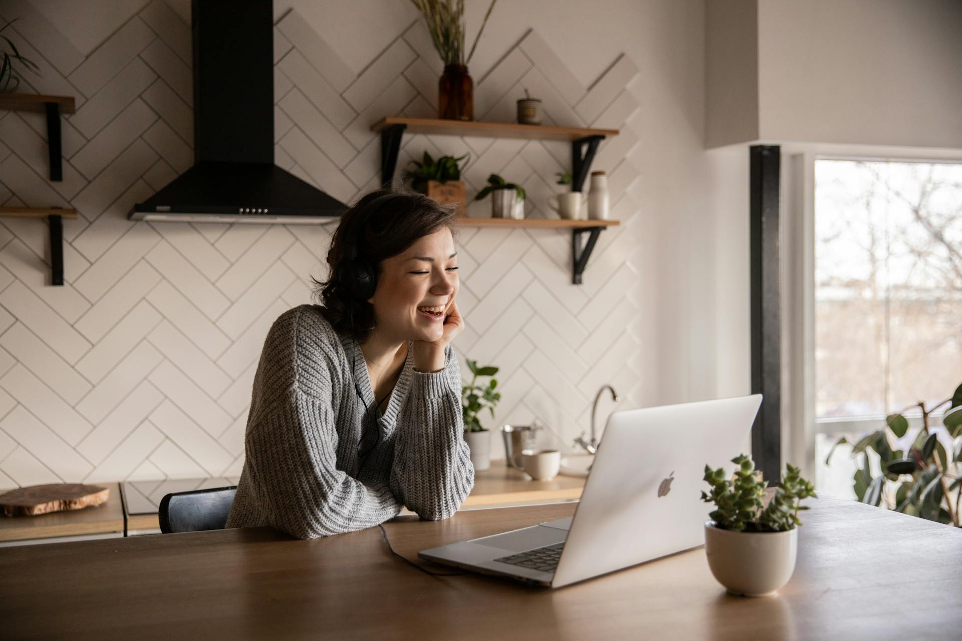 A smiling woman talking via laptop while sitting in the kitchen | Source: Pexels