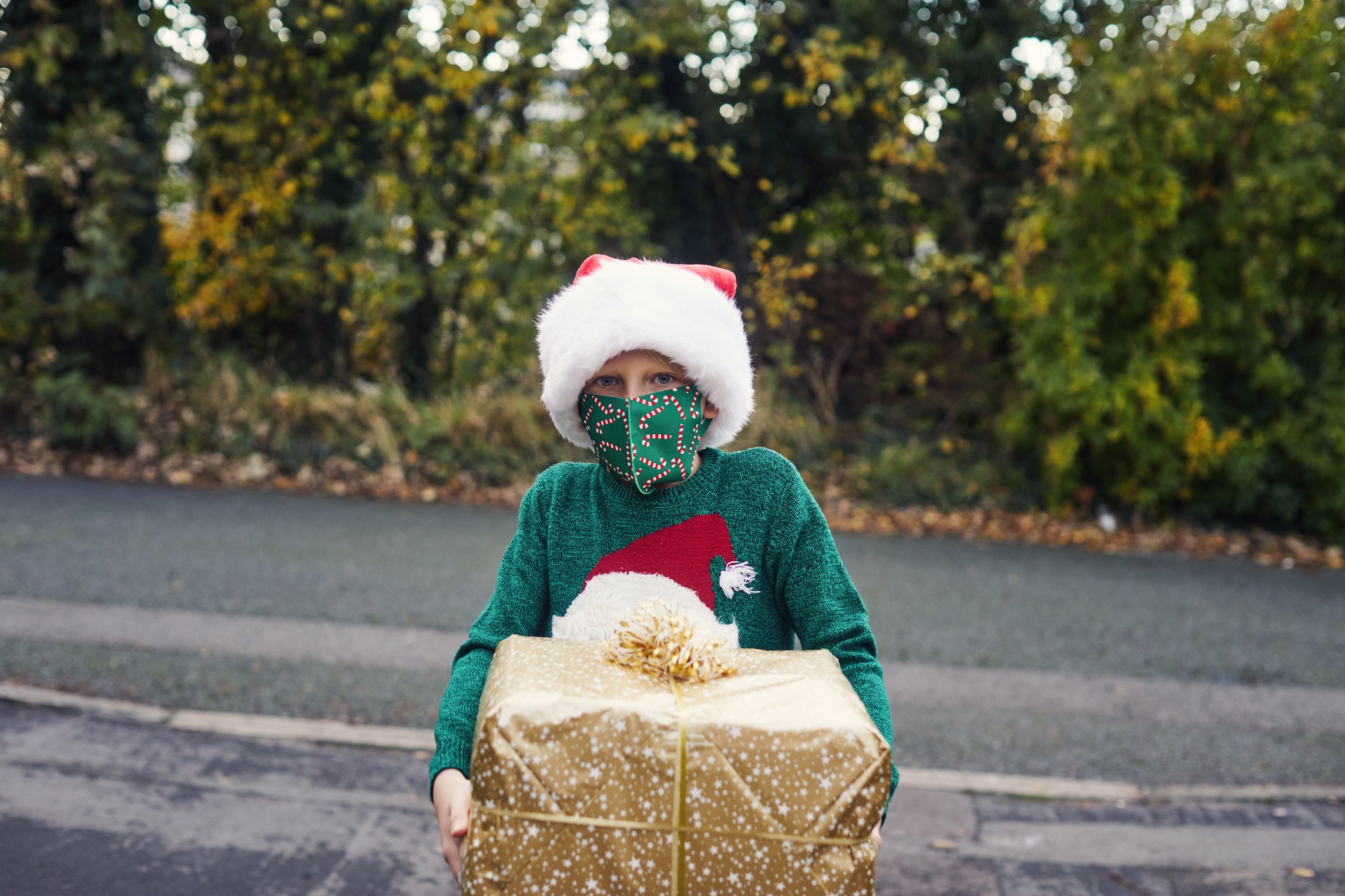 Ein Junge mit einer Weihnachtsmütze und einer Gesichtsmaske, der ein Weihnachtsgeschenk hält. | Quelle: Getty Images