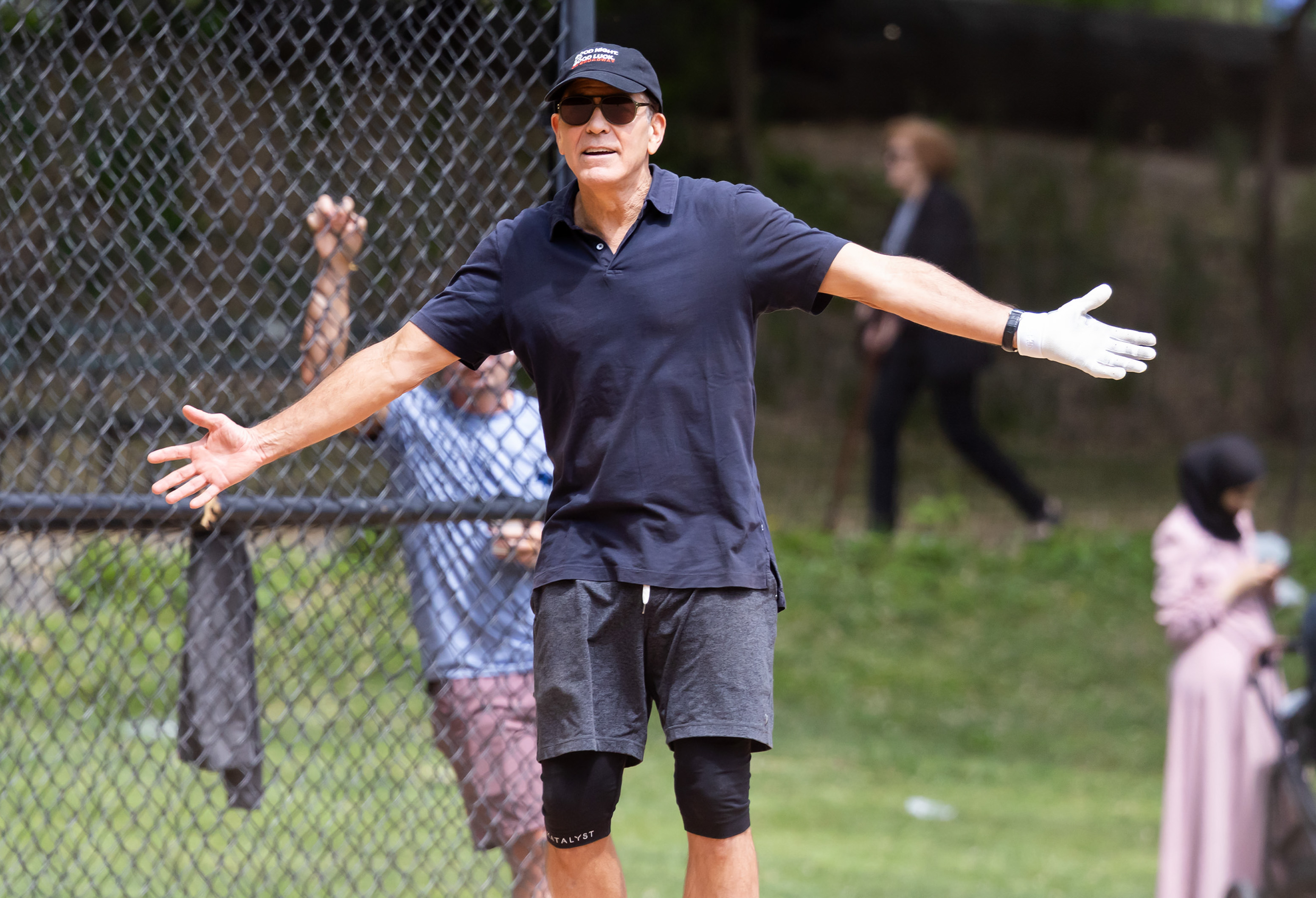 Clooney throws his arms wide in a playful, animated gesture, clearly caught up in the energy of the game. His expression shows amusement and mock disbelief, adding a burst of personality to the moment.