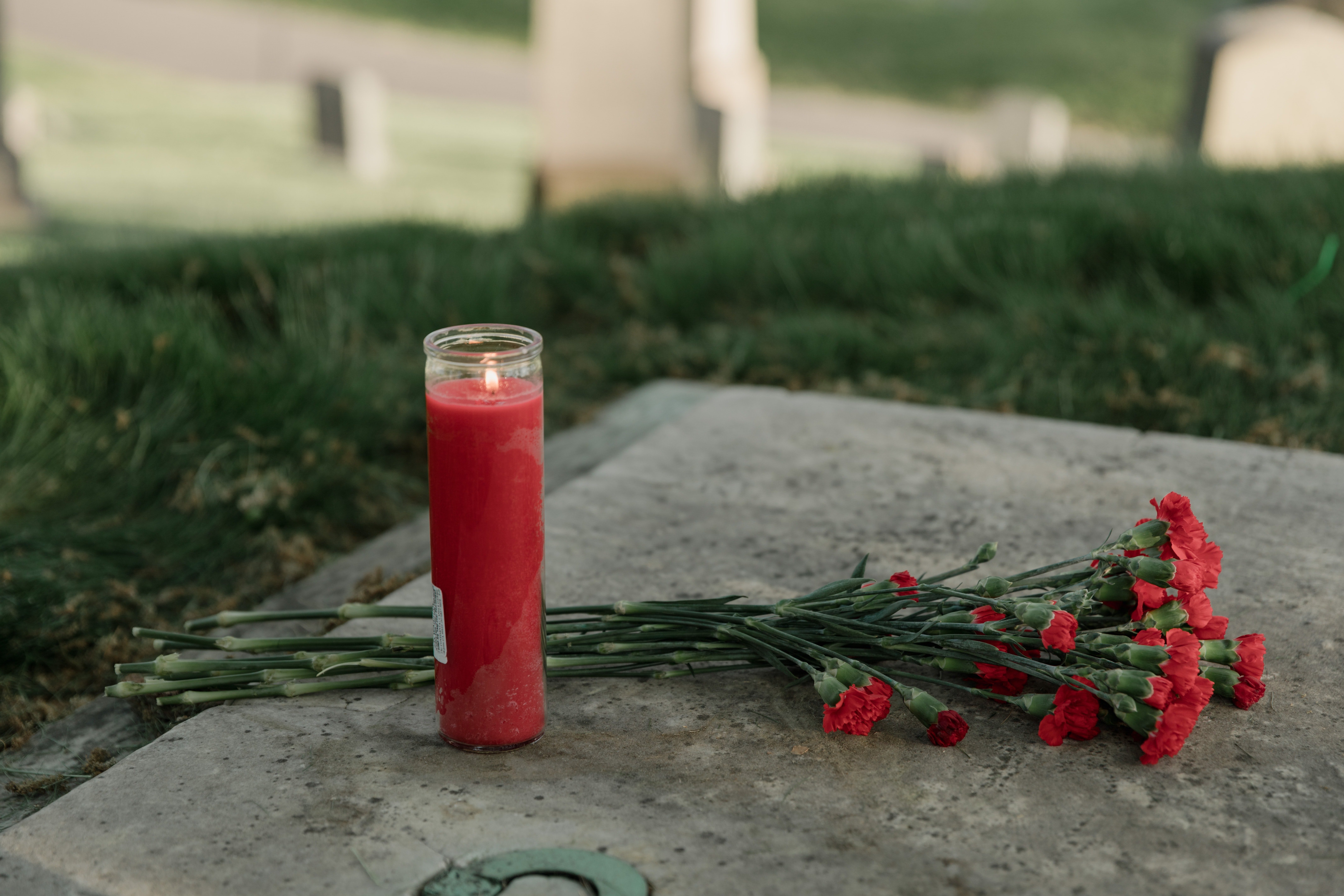 Tumba con flores y vela roja. | Foto: Pexels