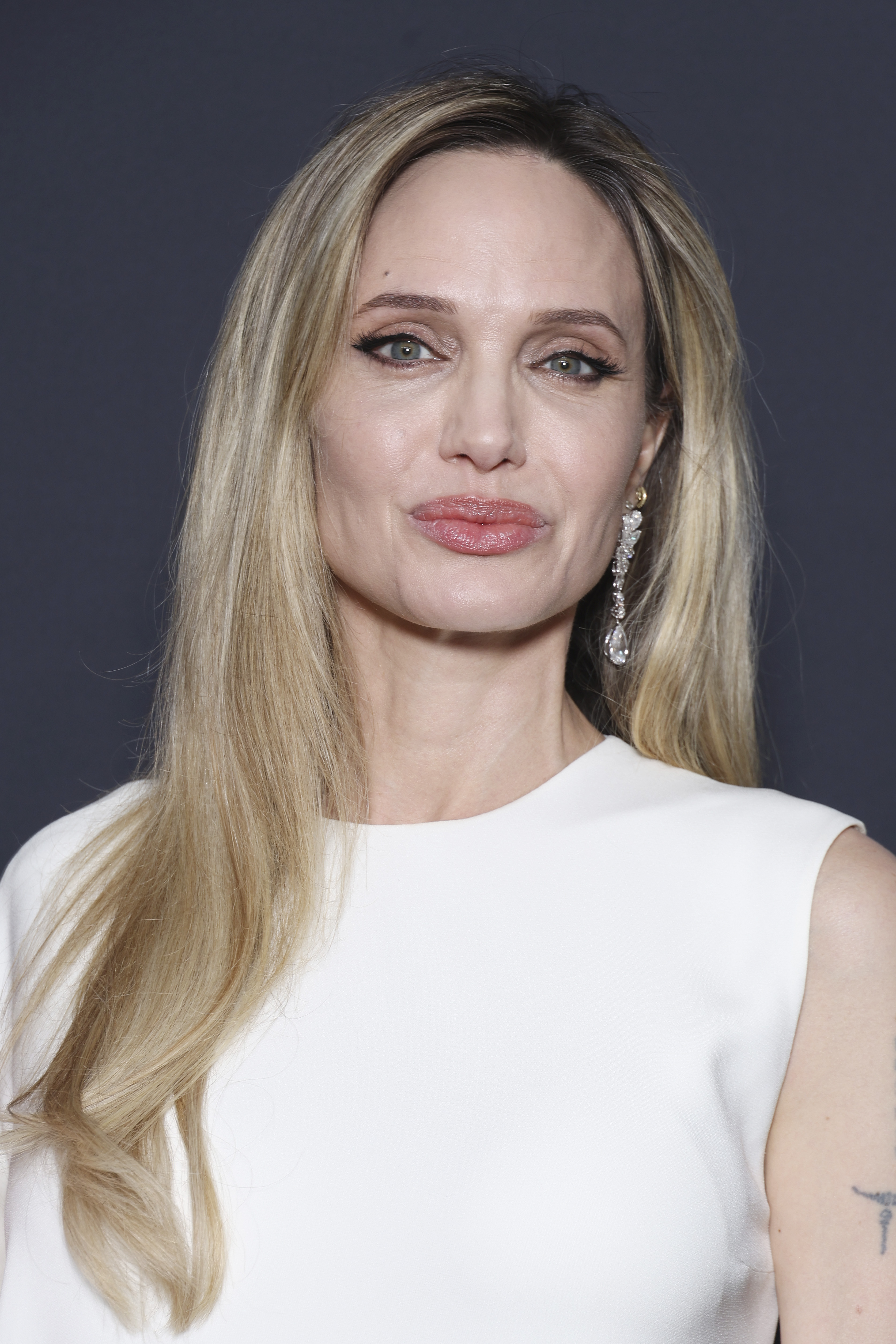 Angelina Jolie is captured in a close-up at the Chopard Trophy photocall, highlighting her soft glam makeup, radiant skin, and shimmering earrings.