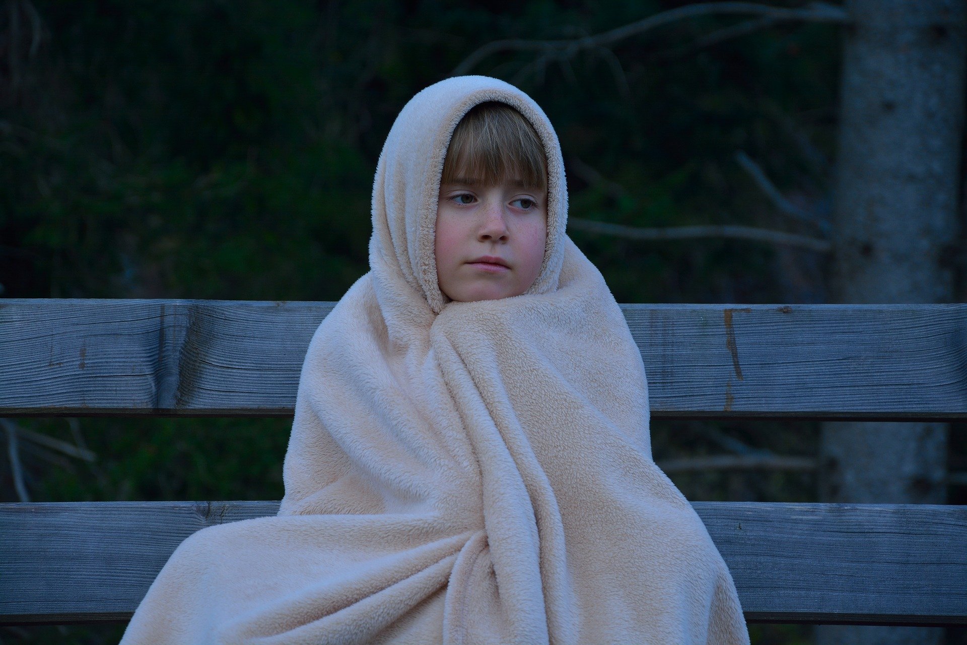 A child wearing a blanket sitting on top of a bench | Source: Pixabay
