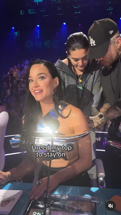 A screenshot shows Katy Perry calmly seated as staff from the "American Idol" show fix her"tin man"-inspired outfit. | Source: Instagram/katyperry