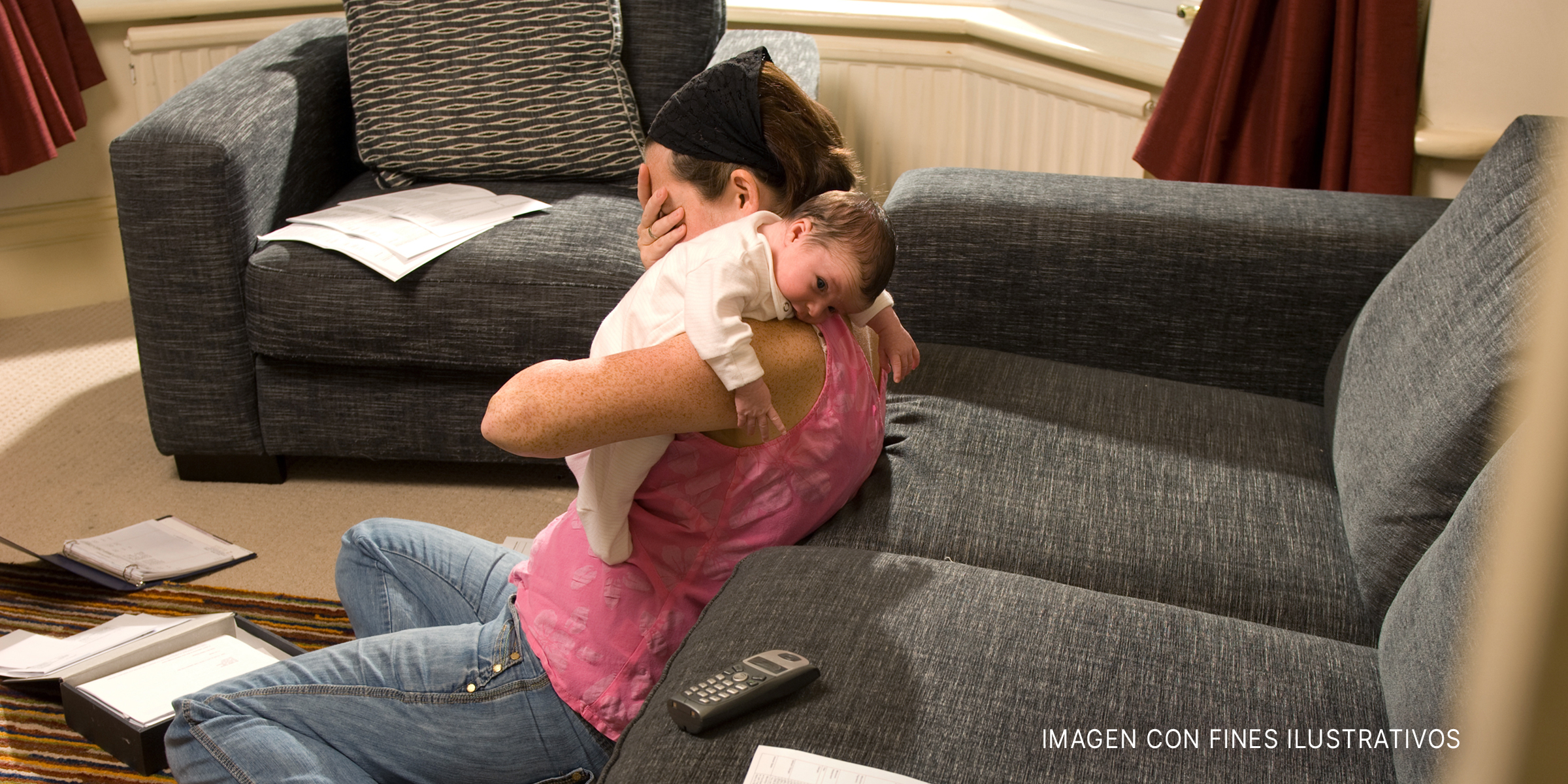 Mujer sentada en el suelo sostiene un bebé y se cubre el rostro con una mano. | Foto: Getty Images