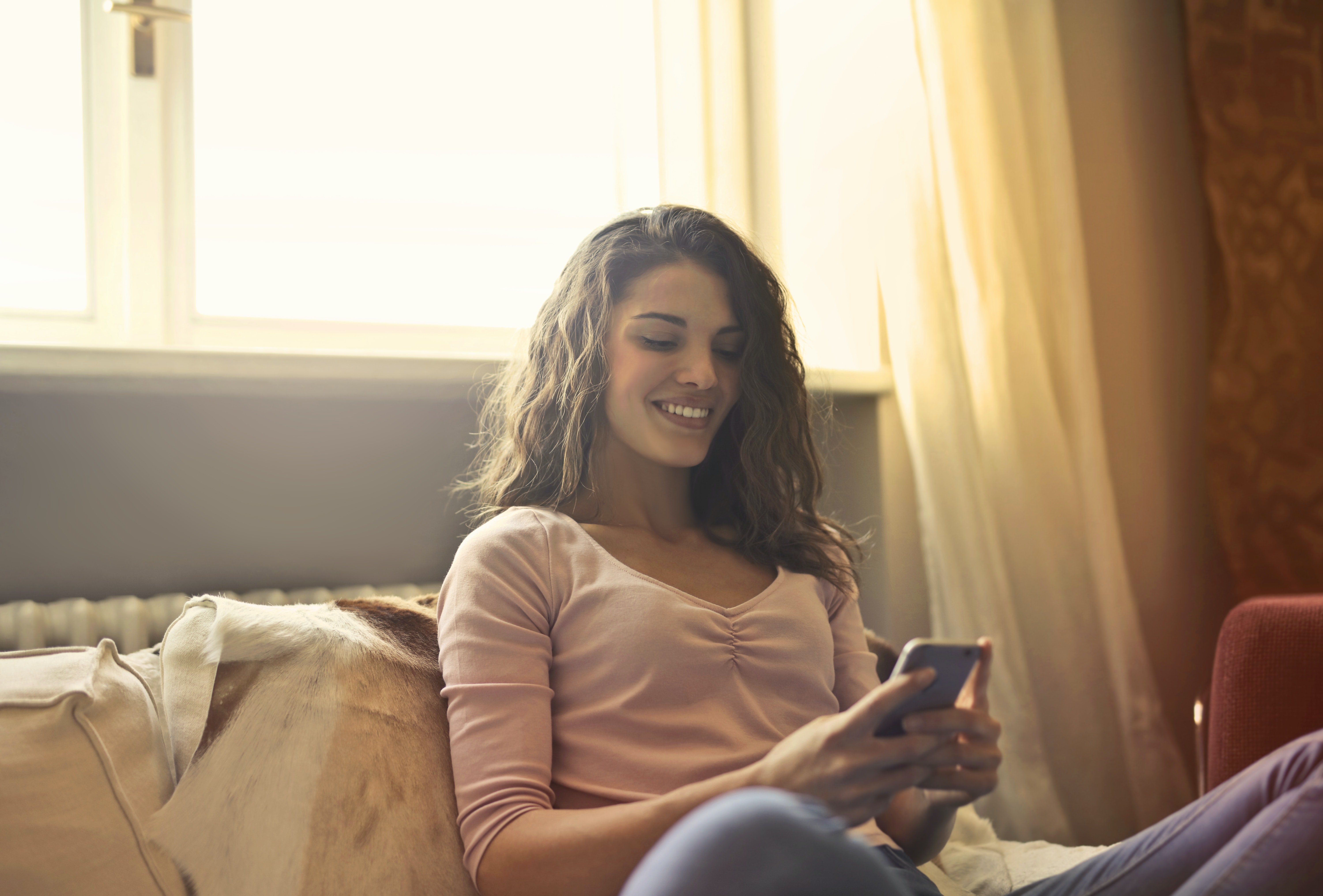 Una mujer sonrie feliz al ver la pantalla de su celular. | Foto: Pexels