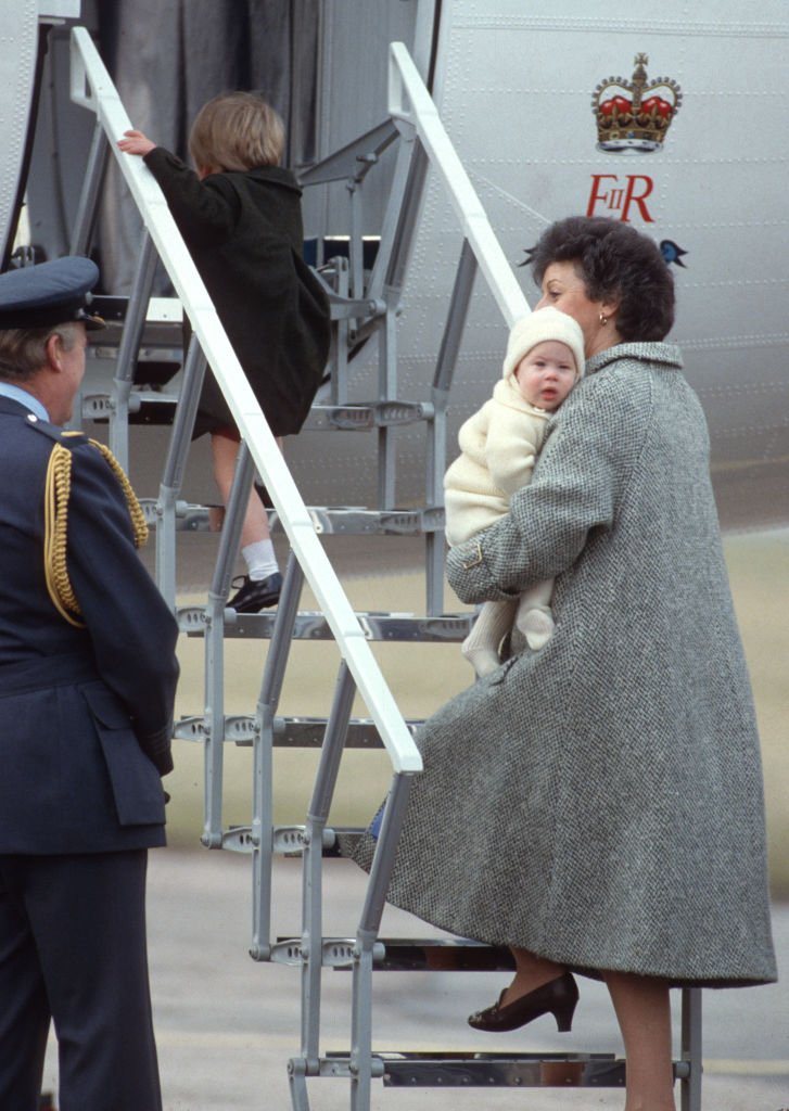 El príncipe William y el príncipe Harry junto a su niñera Barbara Barnes, en el aeropuerto de Aberdeen, Escocia, el 25 de marzo de 1985. | Foto: Getty Images