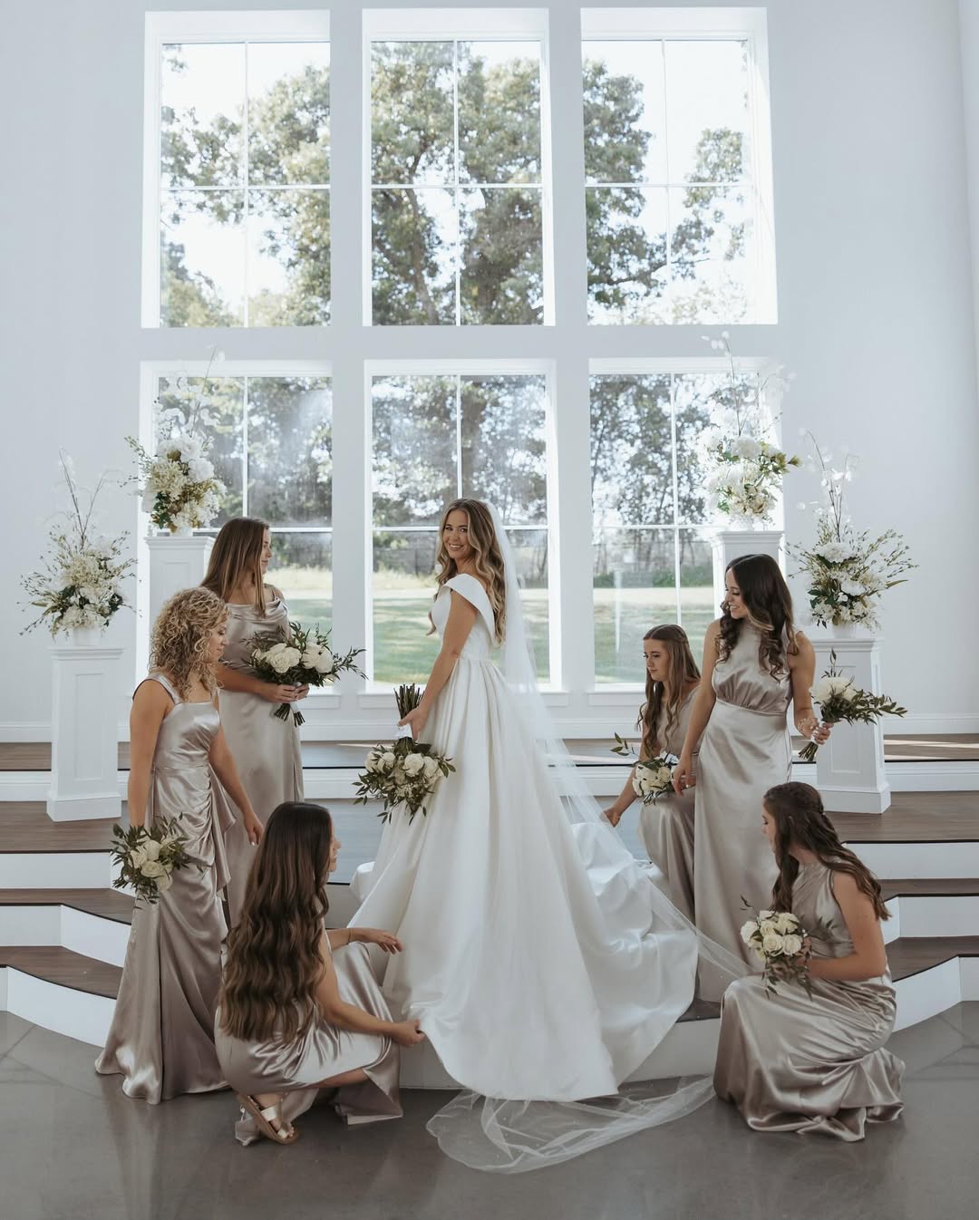 Surrounded by her bridesmaids in soft satin dresses, Jana Duggar stands glowing in her wedding gown, the grand windows framing the elegant moment. | Source: Instagram/janamduggar
