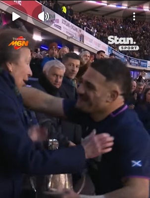 Caught in motion, the captain leans in with arms beginning to lift, seemingly moving towards an instinctive embrace as Princess Anne maintains her footing beside the polished Calcutta Cup. The split second reveals the emotional high of victory meeting royal formality under the bright Murrayfield lights. | Source: YouTube/StanSportAU