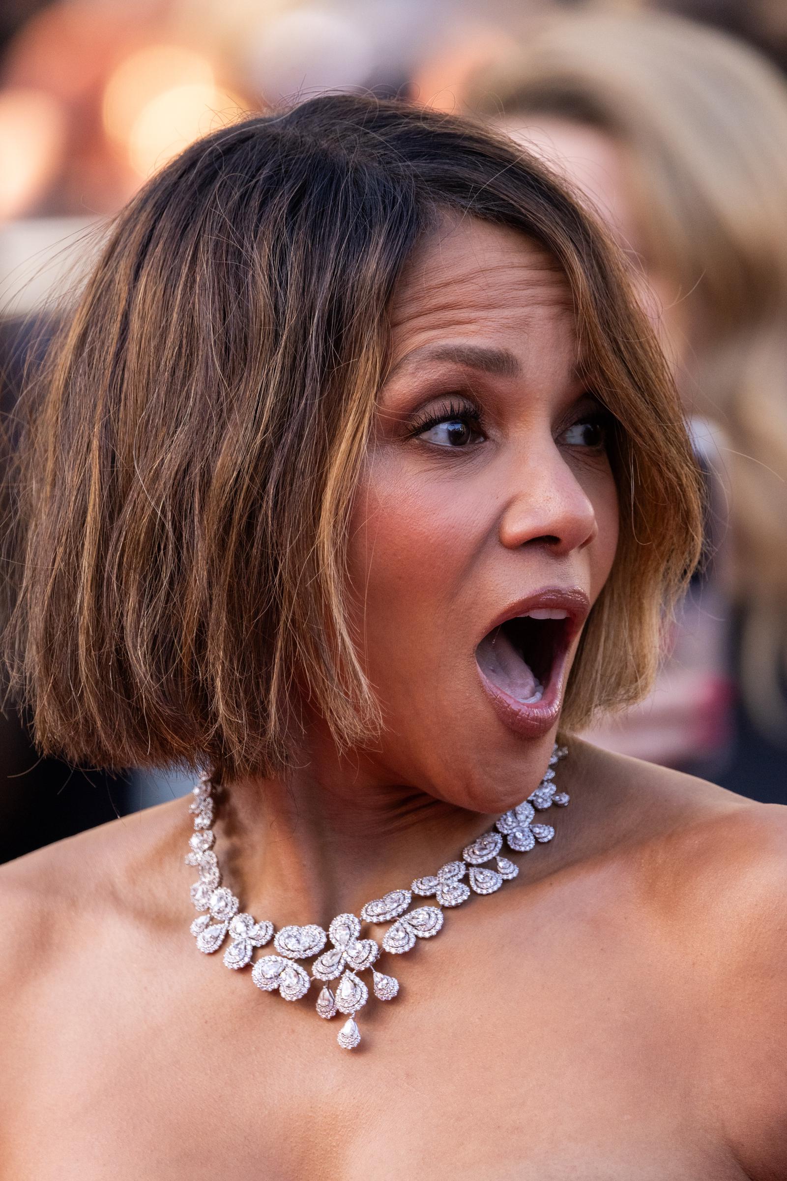 Halle Berry reacts with a surprised expression while on the red carpet at Cannes. Her glam look featured soft neutral makeup, voluminous lashes, and a sleek chin-length bob with subtle highlights.