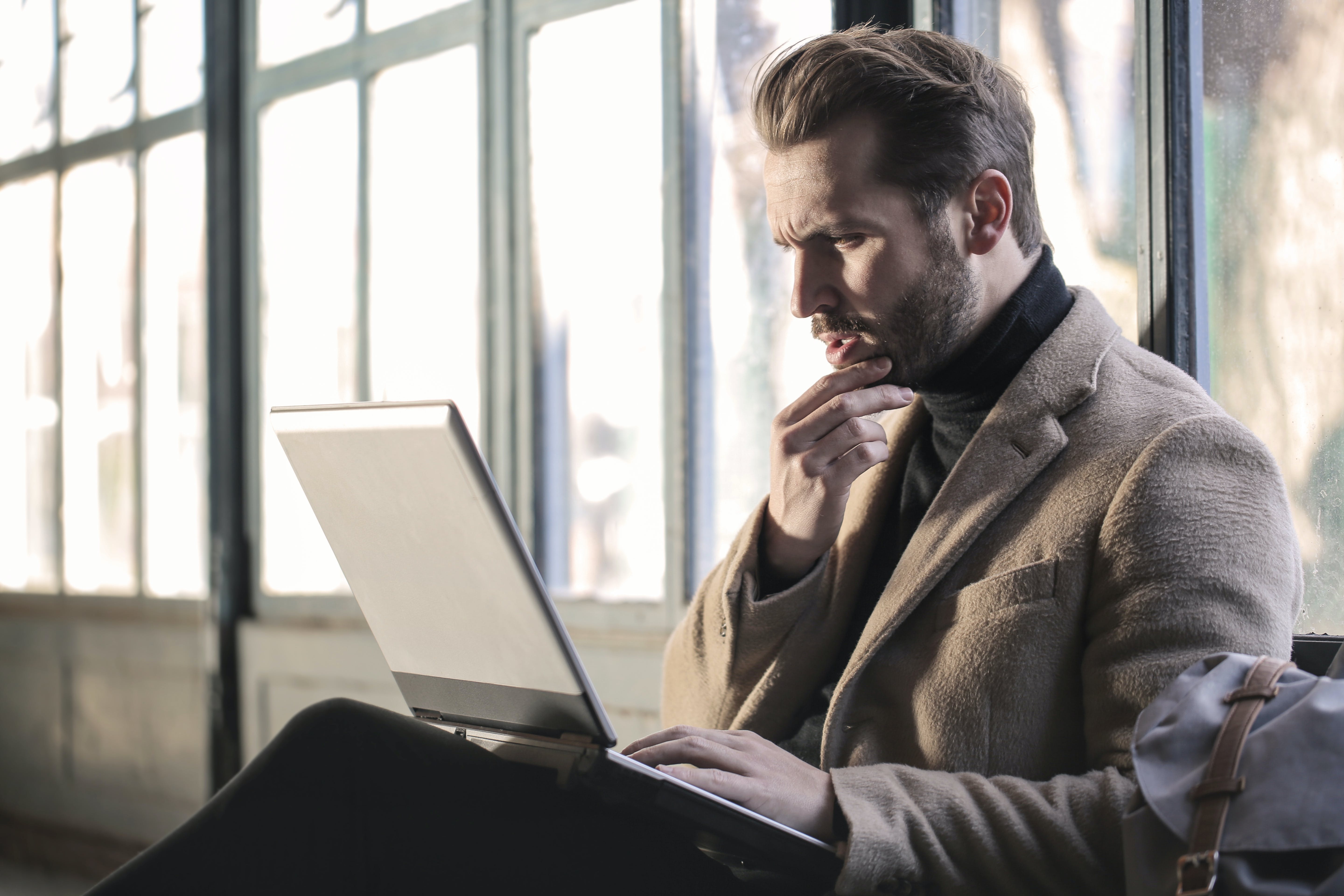 A confused man holding his chin while seated looking at a laptop | Source: Pexels