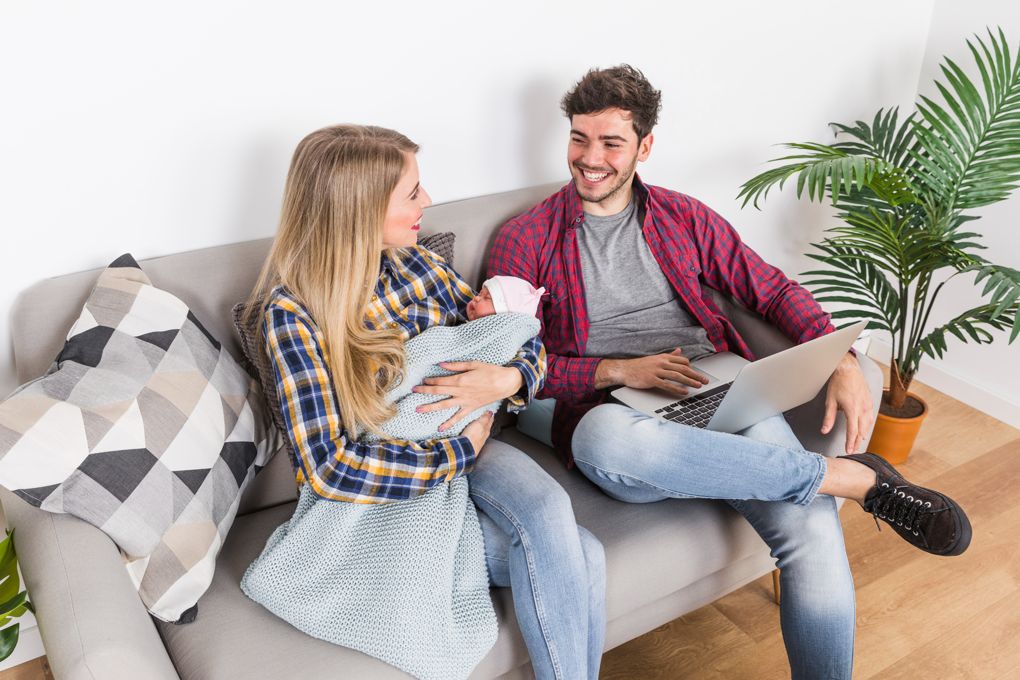 A woman with a baby looks at her husband who's using a laptop | Source: Freepik