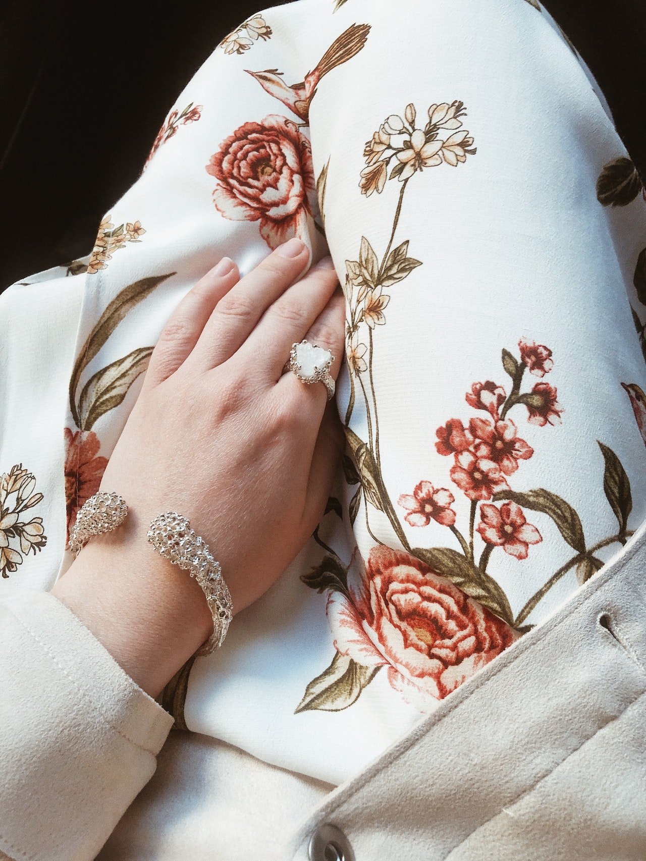 Mujer luciendo un brazalete y un anillo con su mano sobre la tela de su falda floreada. | Foto: Pexels