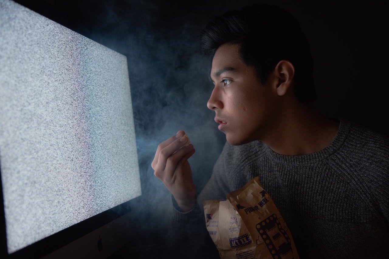 Man eating chips while watching TV| Photo Amateur Hub from Pexels