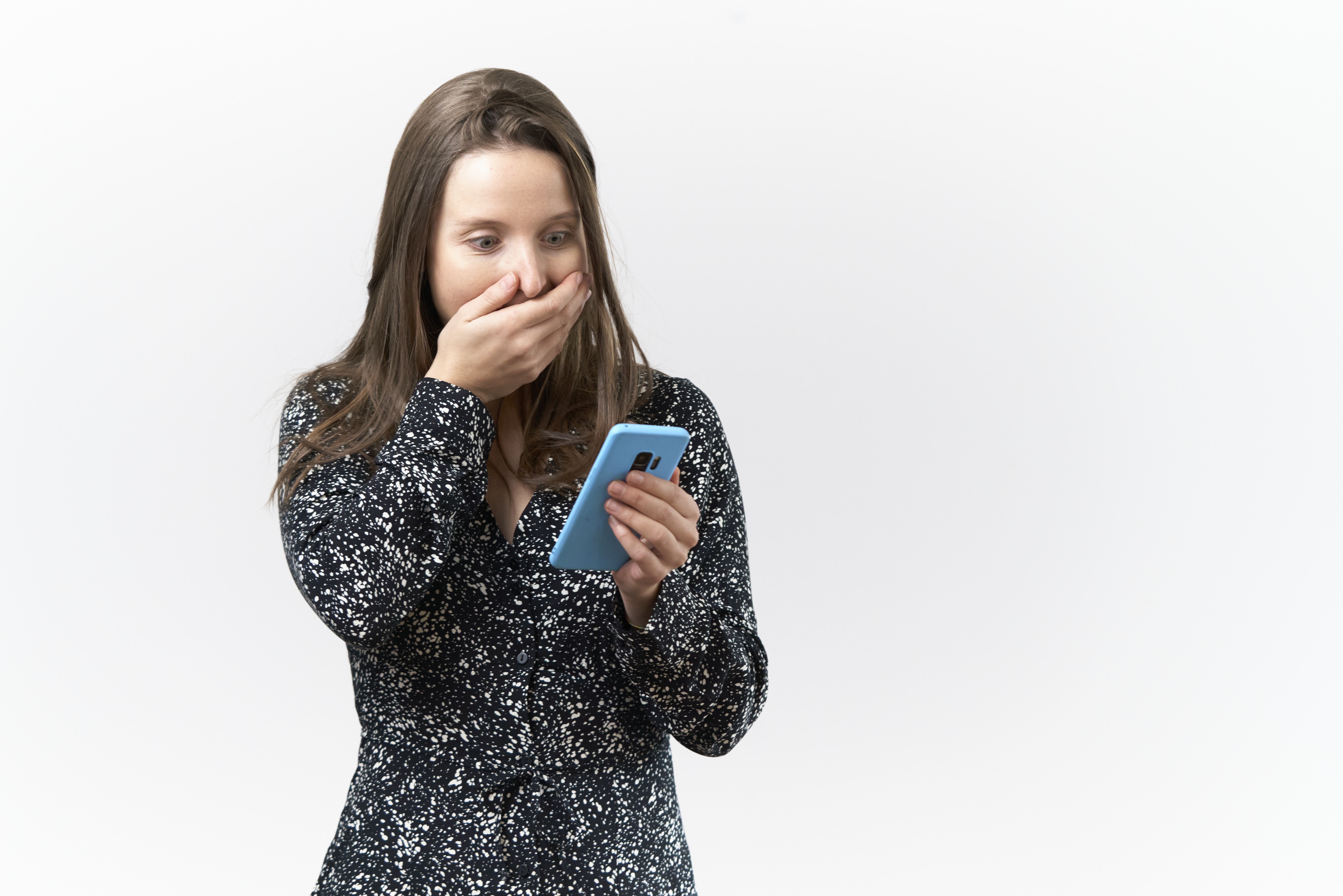 Young woman with surprised expression reading messages on cell phone against white background | Source: Getty Images
