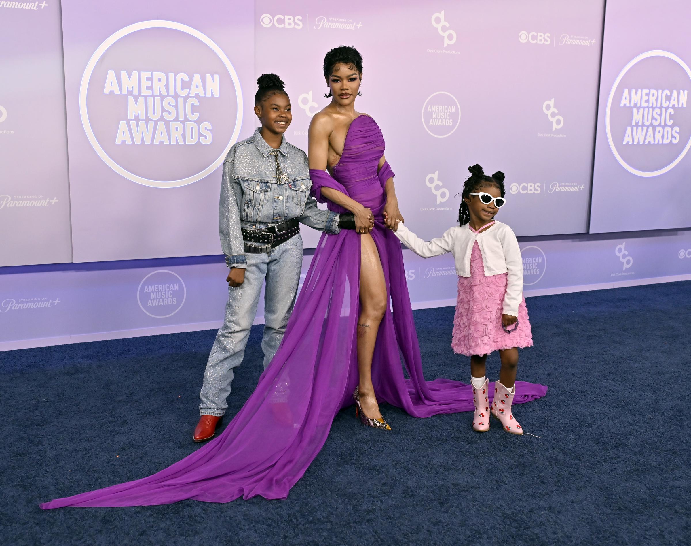 Teyana Taylor poses between her daughters while the long purple train of her gown spreads across the arrivals area | Source: Getty Images
