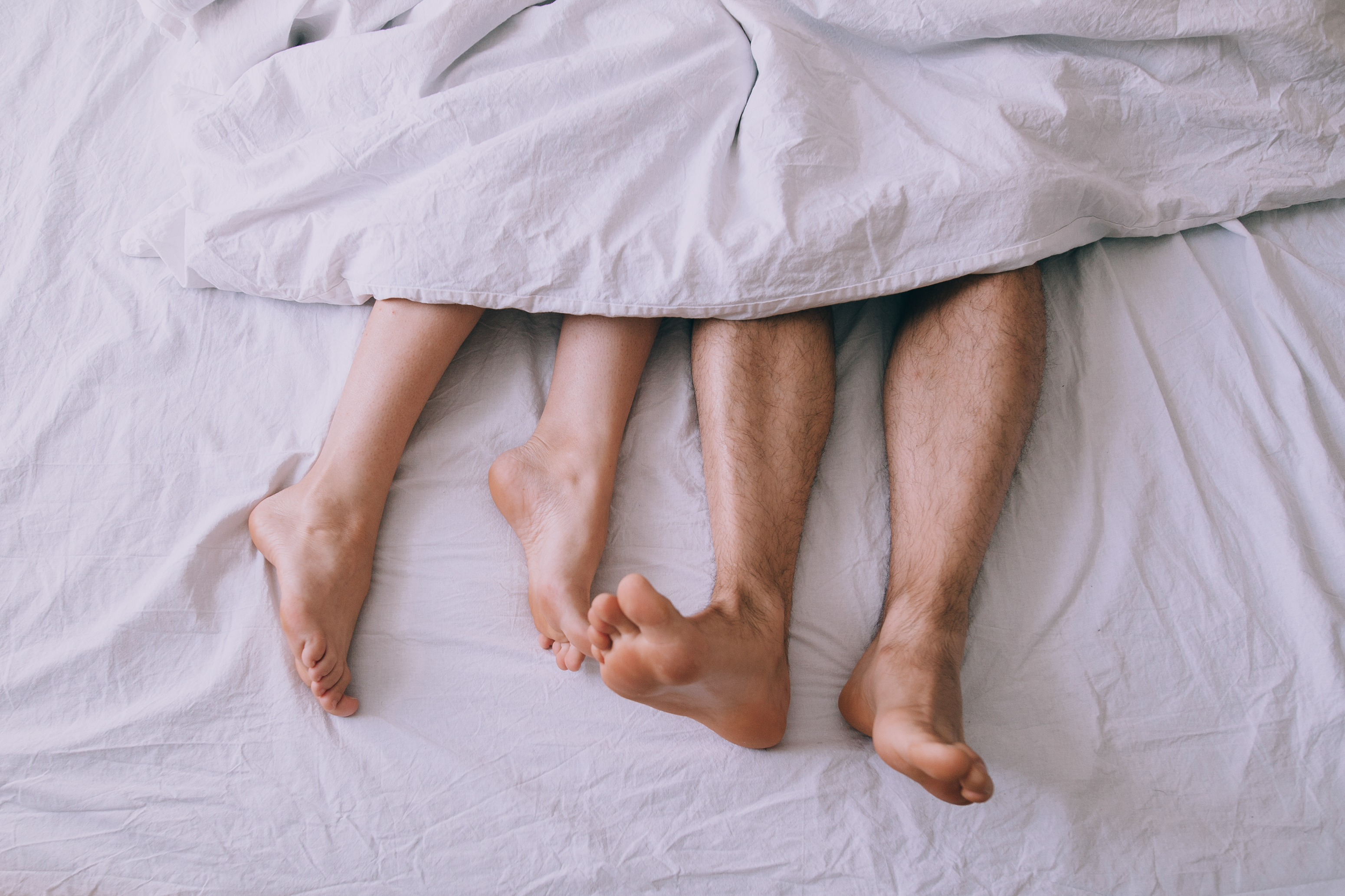 Feet of couple side by side in bed | Source: Shutterstock