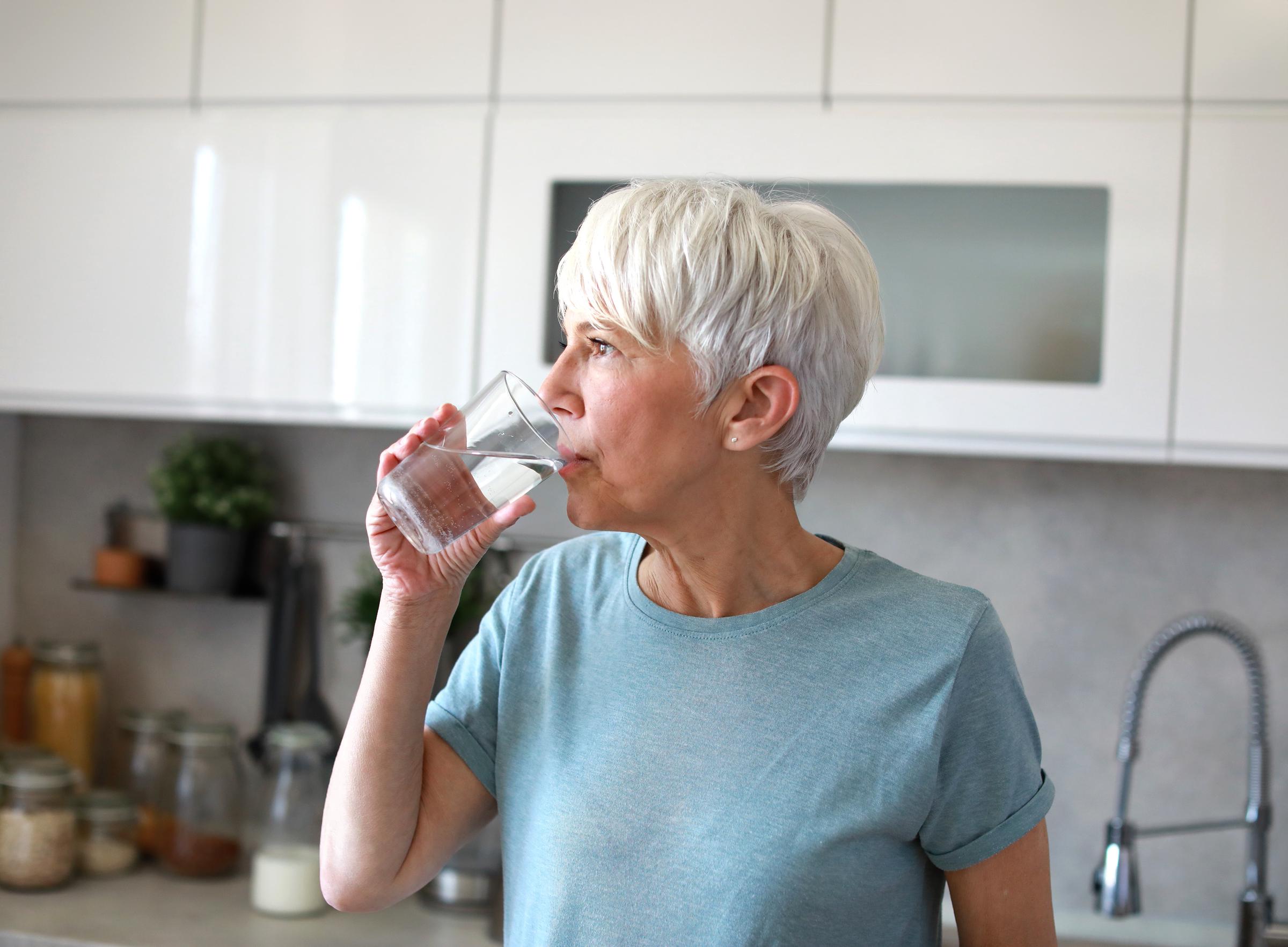 A woman drinking a glass of water in the kitchen | Source: Shutterstock