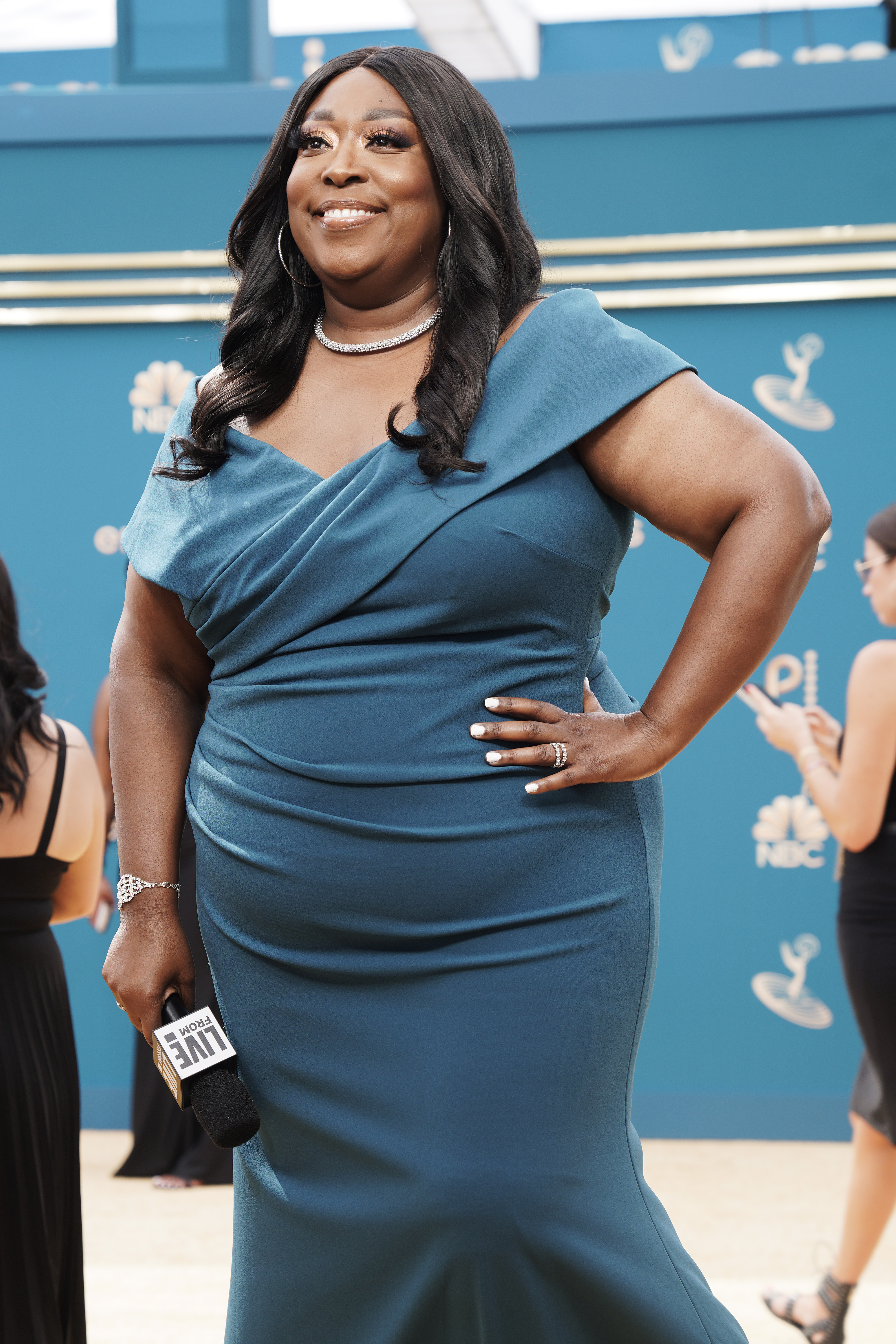 Loni Love visits "E! Live from the Red Carpet" at the 74th Annual Primetime Emmy Awards on September 12, wearing a teal gown and holding a microphone as she smiles at the event.