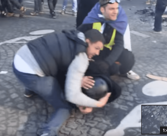 Adel et un Gilet jaune protégeant un policier sur les Champs-Elysées, le 16 mars 2019. | Photo : Youtube/InfoCritiqueWeb