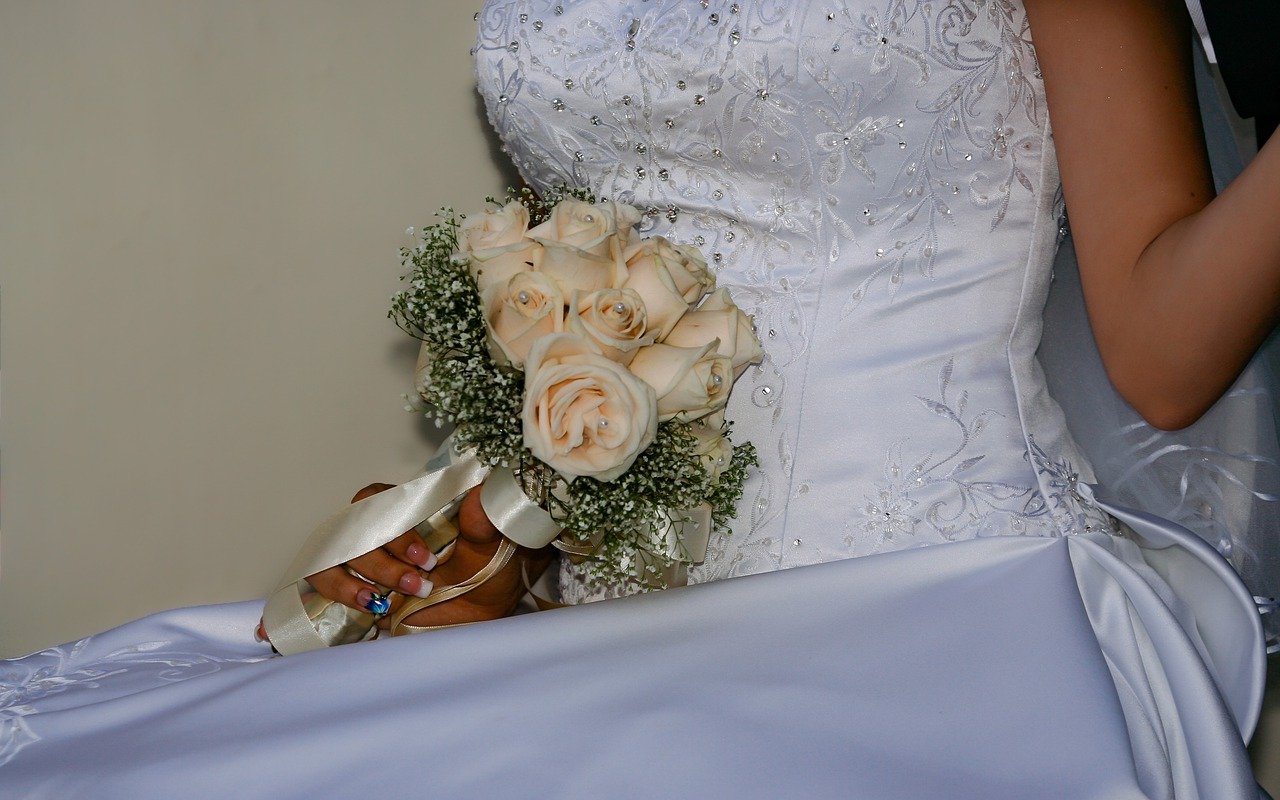 A woman wearing a wedding dress and holding a bouquet of white roses. | Image: Pixabay.