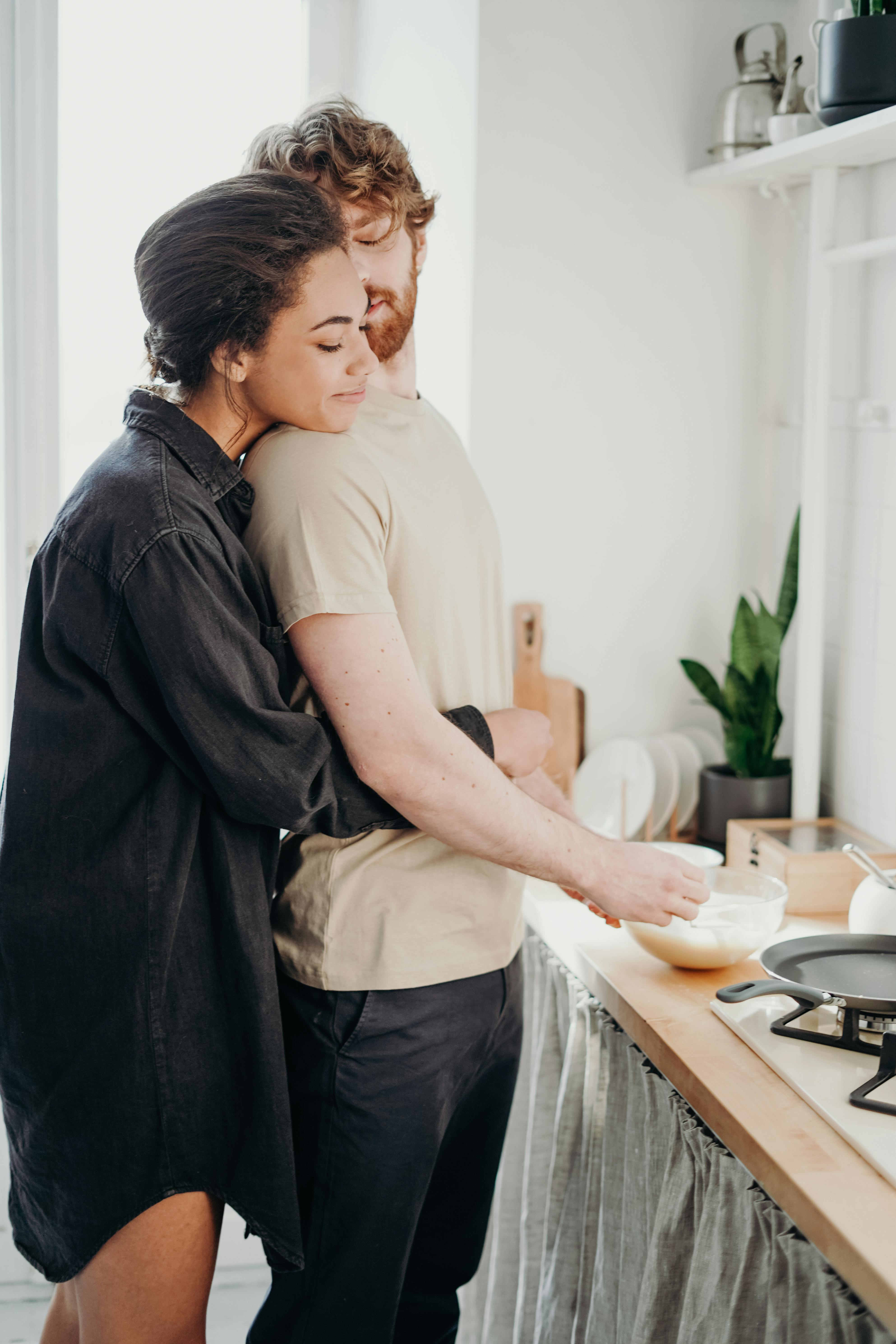 A woman hugging her man while he prepares breakfast | Source: Pexels