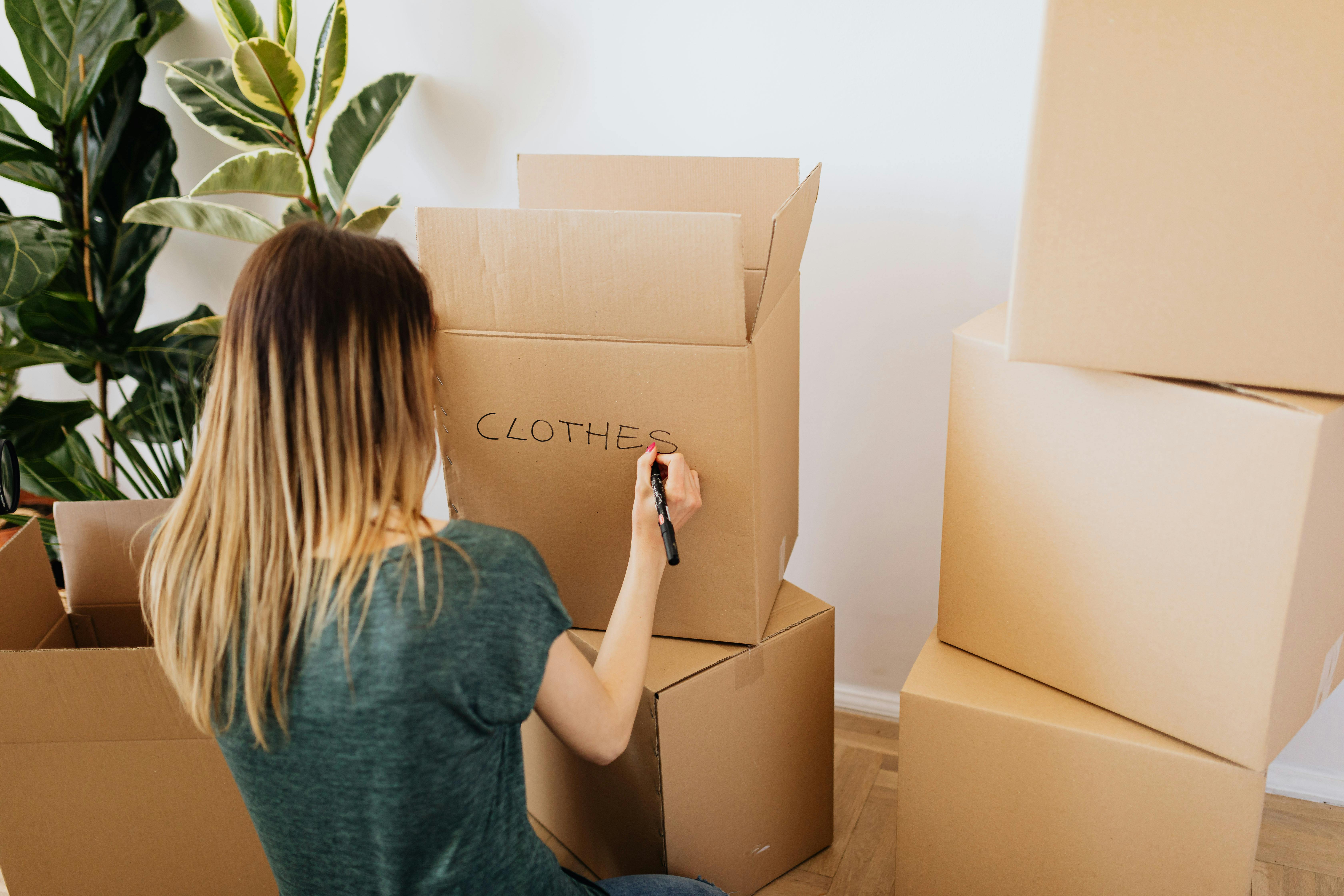 A woman writing the word clothes on a carton box | Source: Pexels