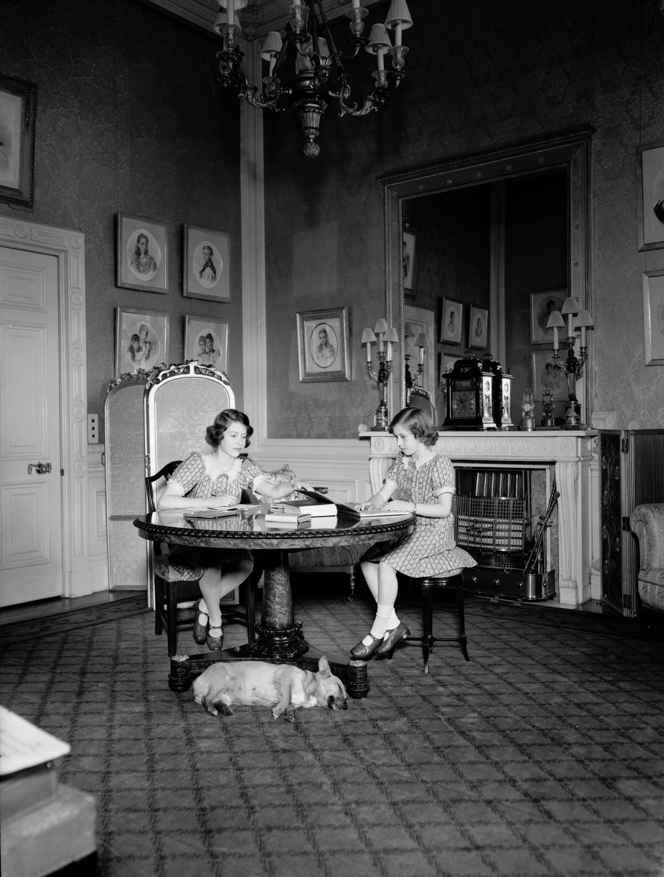 Princesses Elizabeth (left) and Margaret (1930 - 2002) studying whilst a corgi dog sleeps at their feet in a drawing room at Windsor Castle, Berkshire. | Source: Getty Images