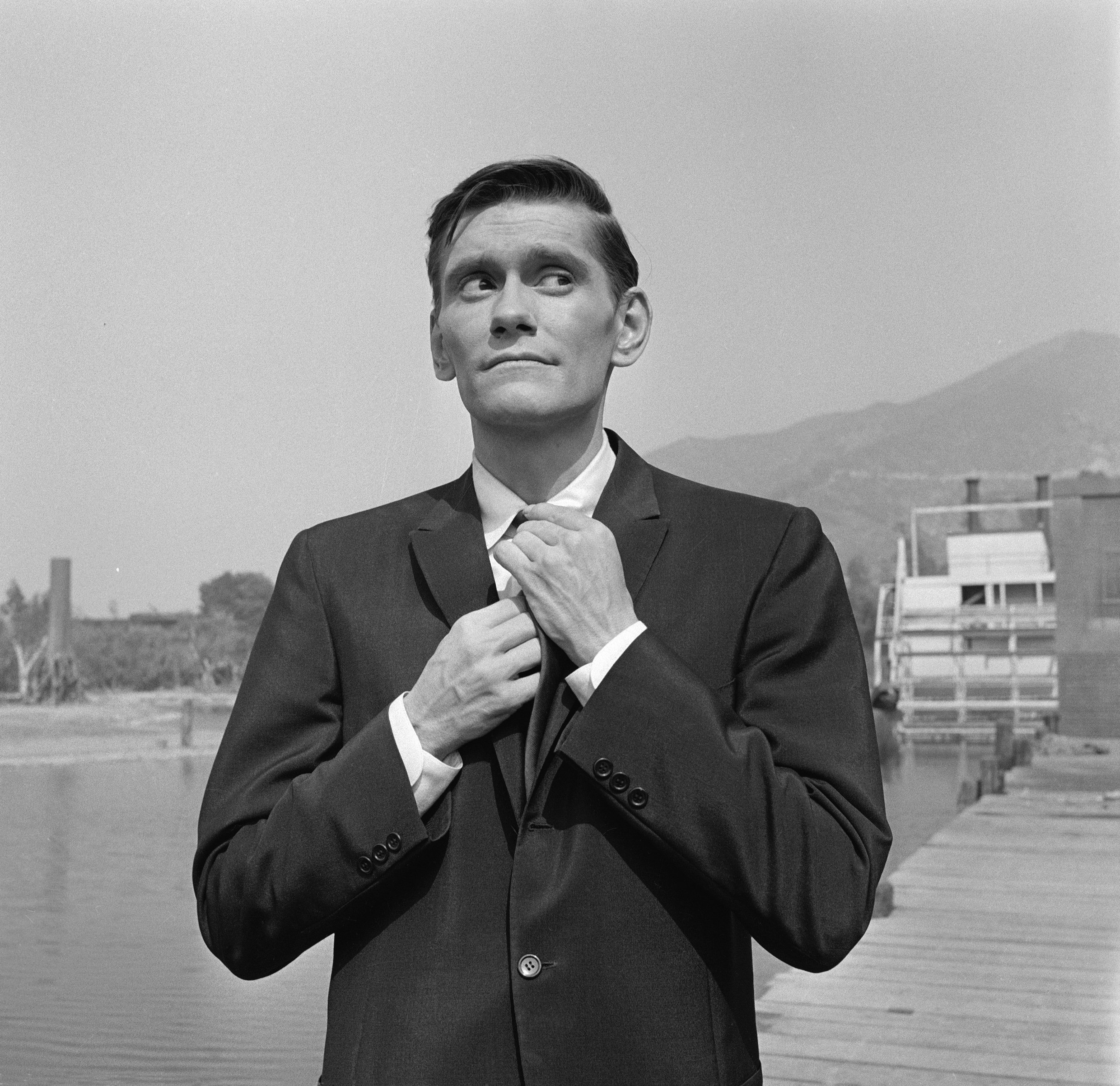American actor Dick York adjusts his necktie as he stands on a wooden dock during the filming of an episode of the television anthology series "The Alfred Hitchcock Presents" entitled "The Blessington Method," on September 3, 1959 | Photo: Getty Images