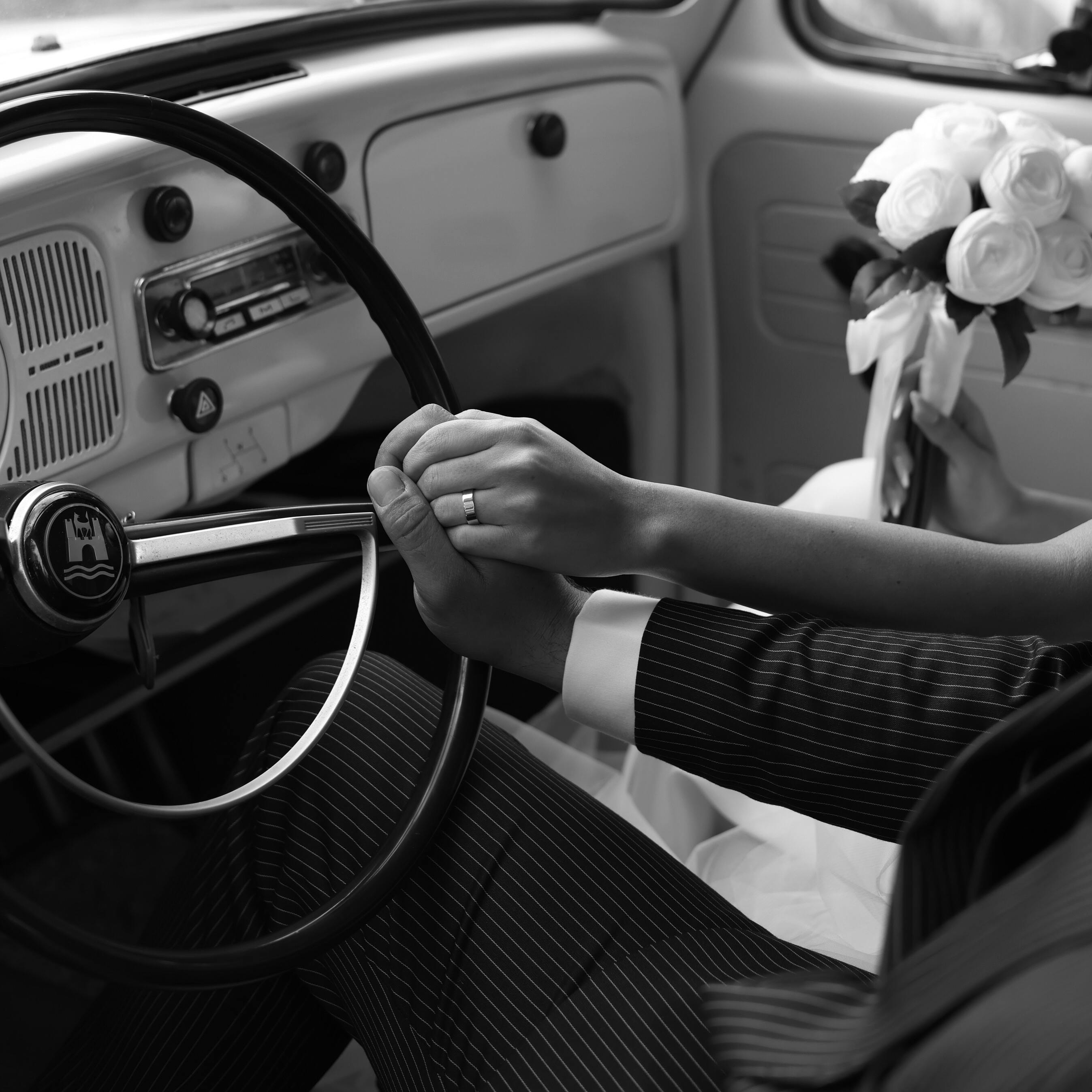 A bride and groom holding hands on a steering wheel | Source: Pexels