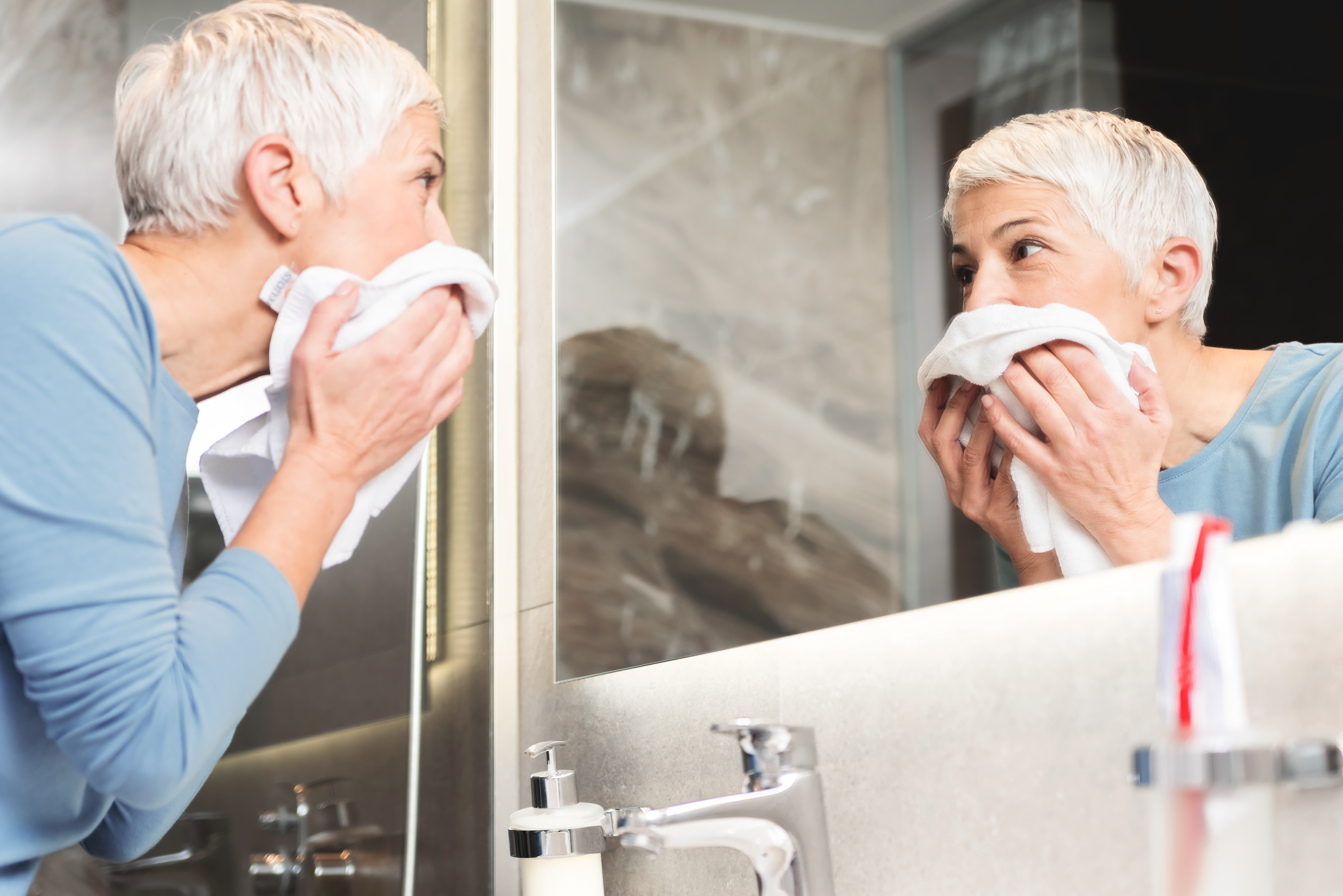 Woman with short, grey hair washing her face | Source: Shutterstock
