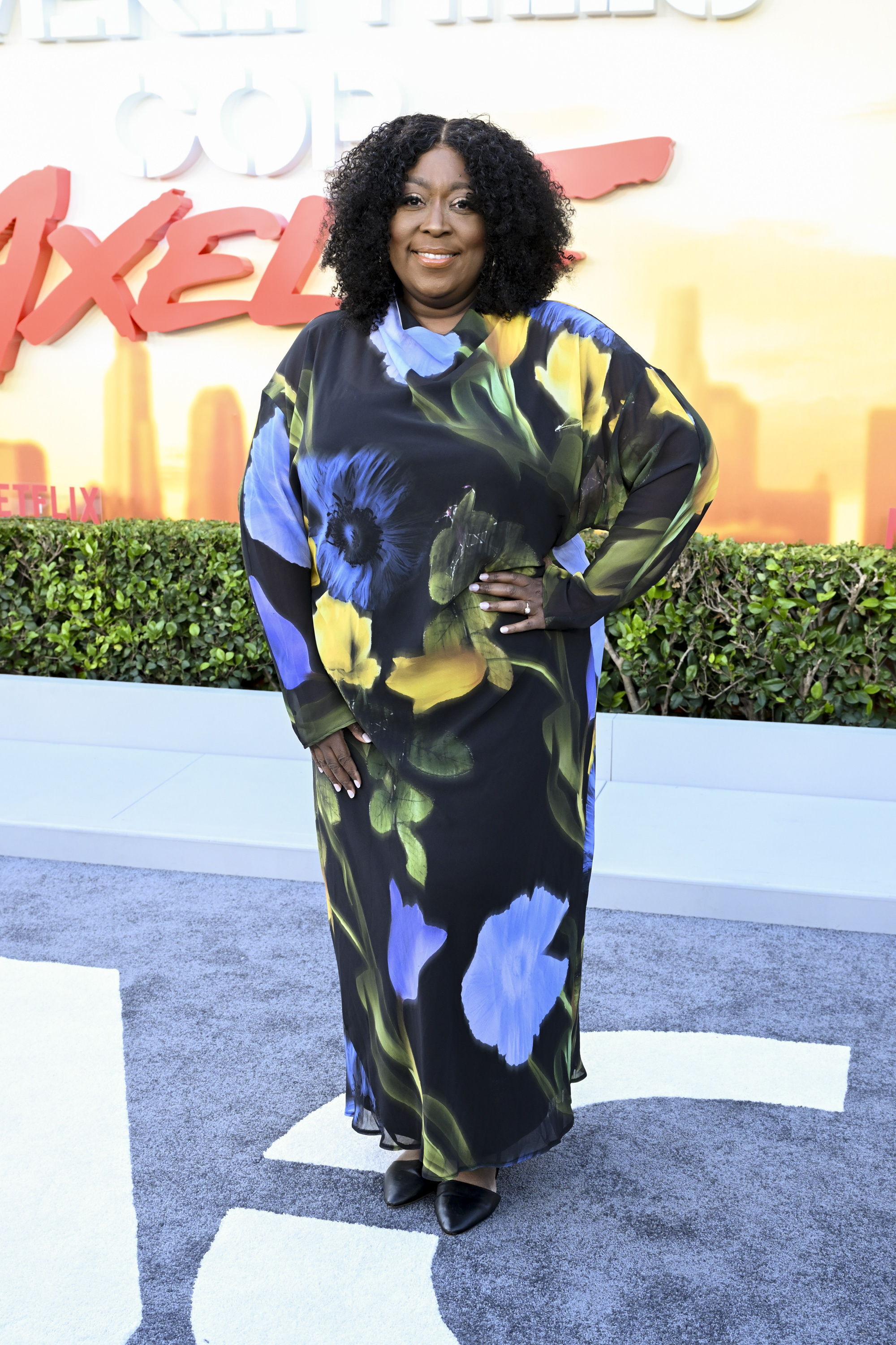 Loni Love attends the "Beverly Hills Cop: Axel F" world premiere on June 20, wearing a flowing floral-print dress and black heels as she poses before the film's bright backdrop.