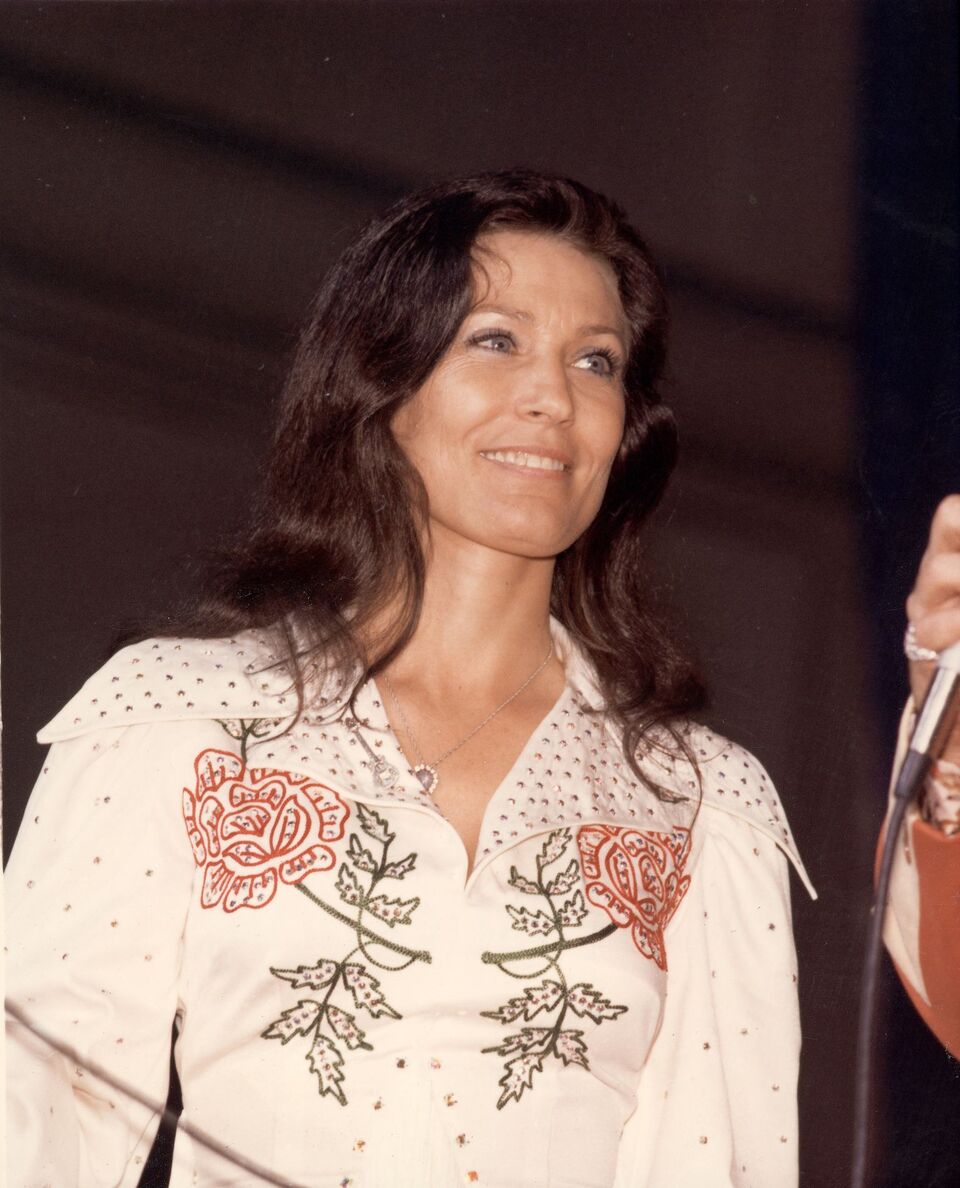 Loretta Lynn smiles as she looks at an unidentified person off-camera who holds a microphone, late 1970s. | Source: Getty Images