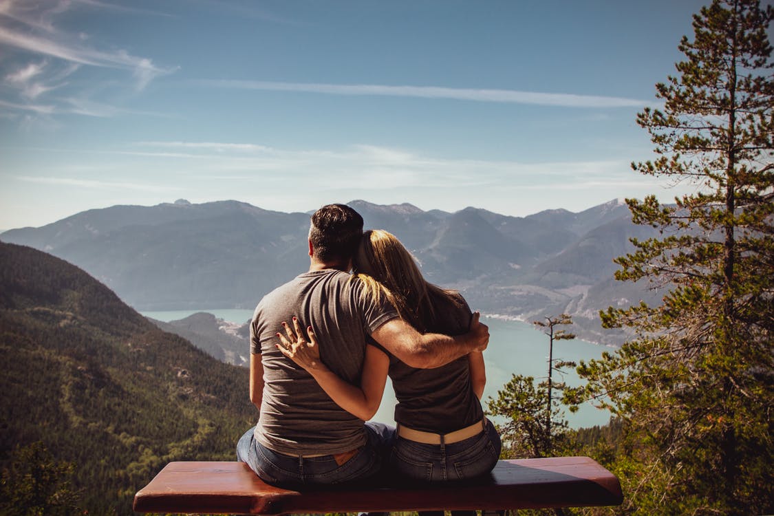 Una pareja sentada mirando las montañas y un lago. | Foto: Pexels