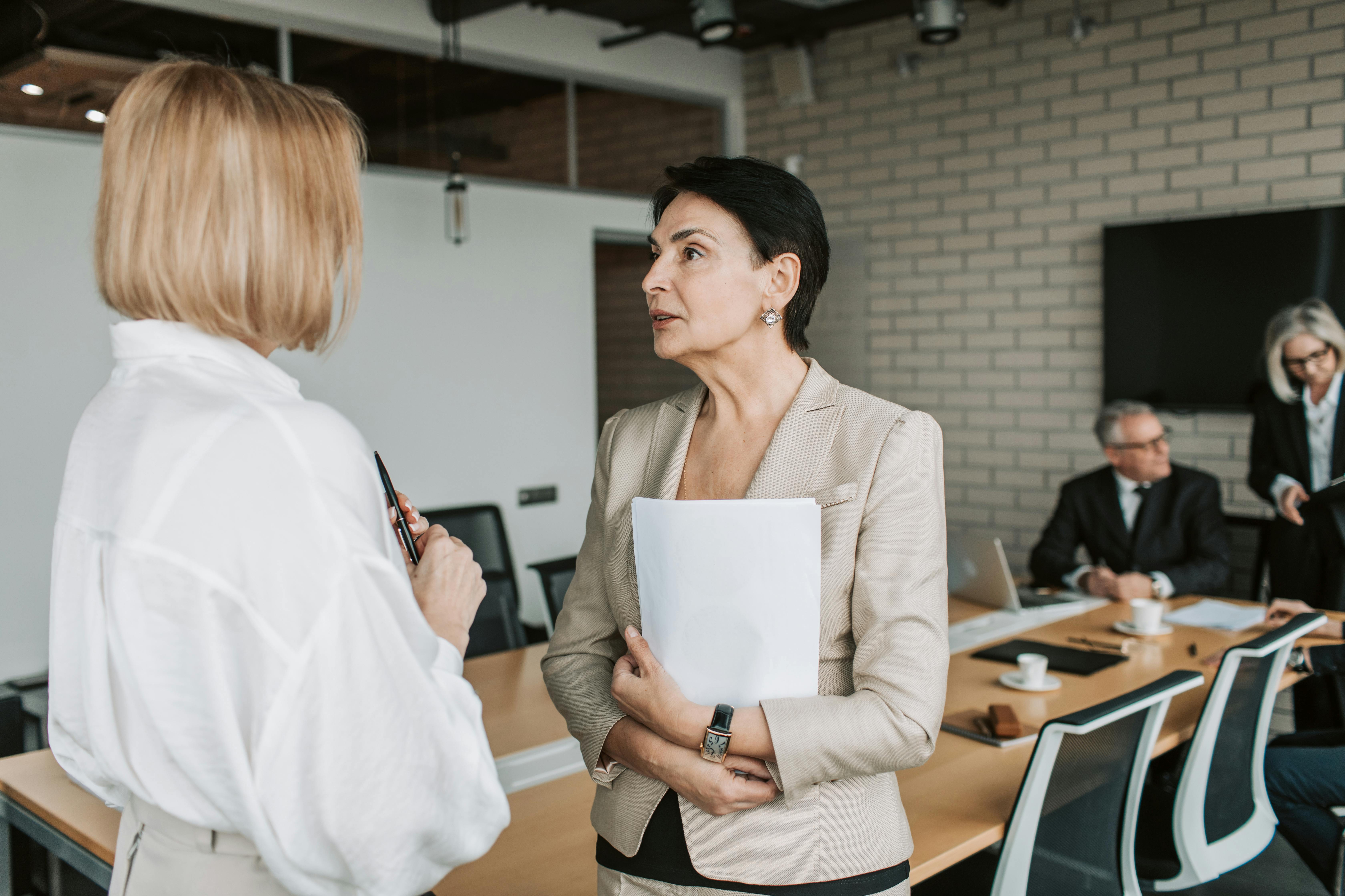 Two women talking in a boardroom while others appear in the background | Source: Pexels