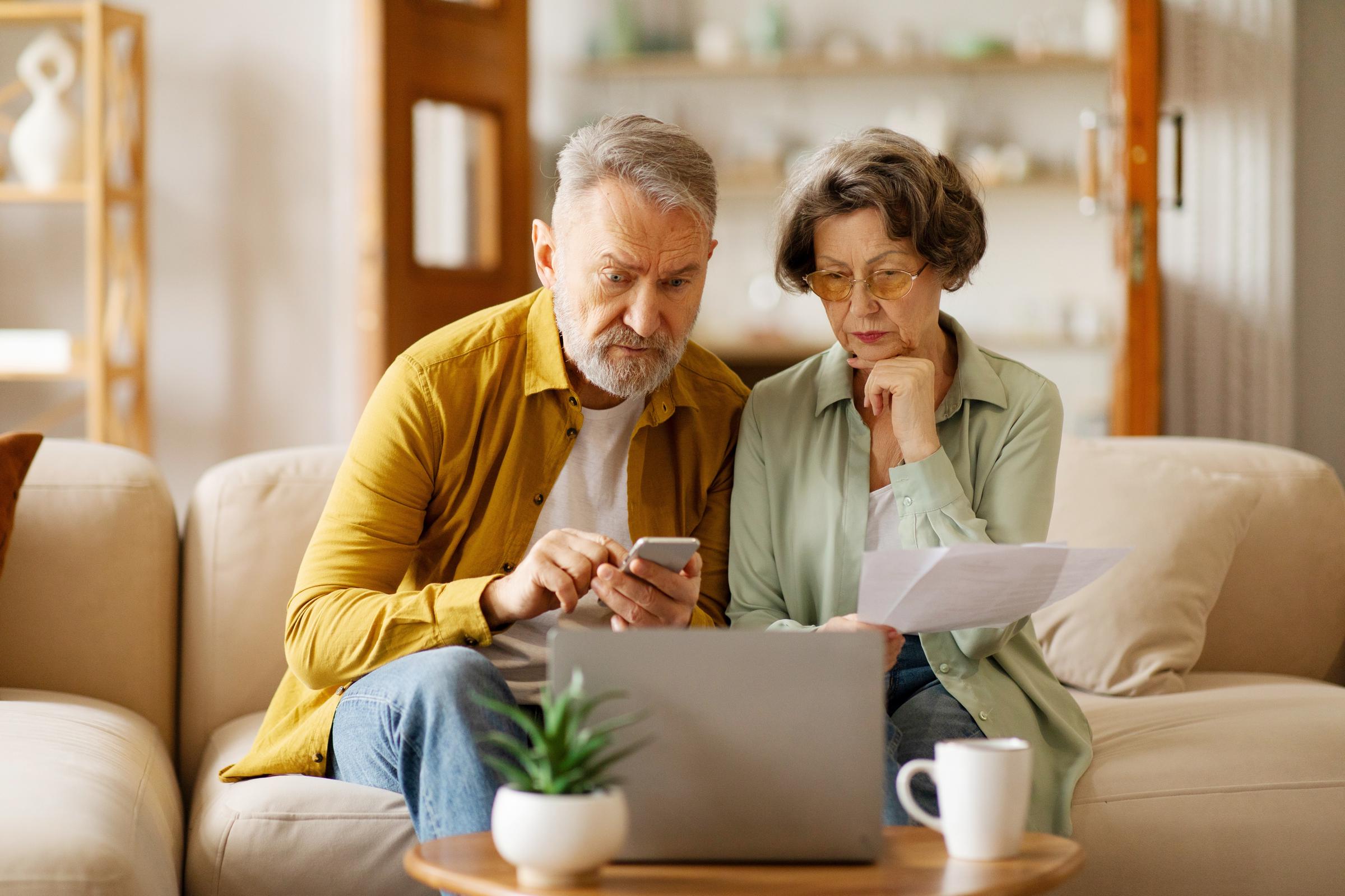 A senior couple managing their finances with a laptop and on mobile | Source: Shutterstock