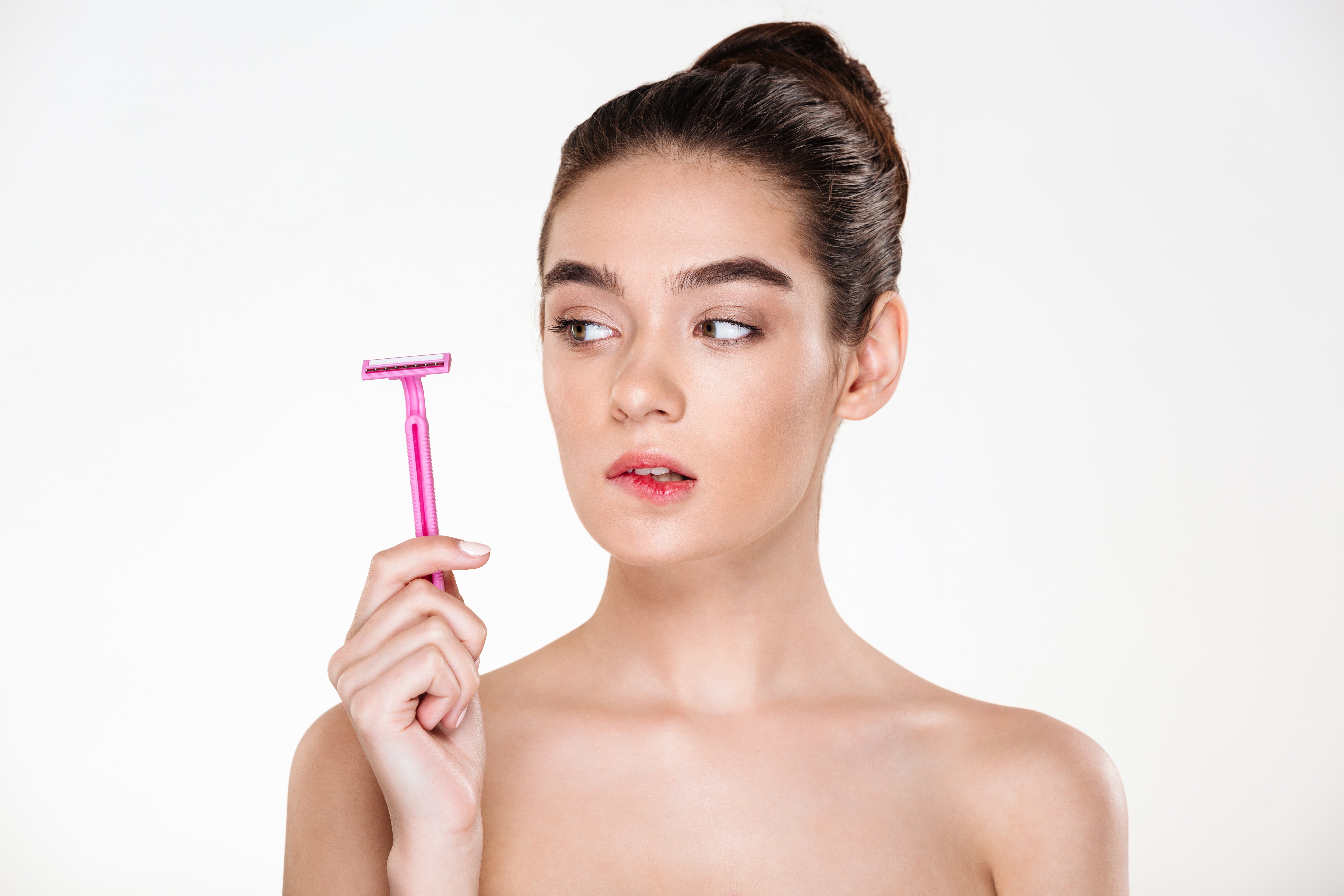 An unhappy woman looking at pink razor in her hand. | Photo: Shutterstock.