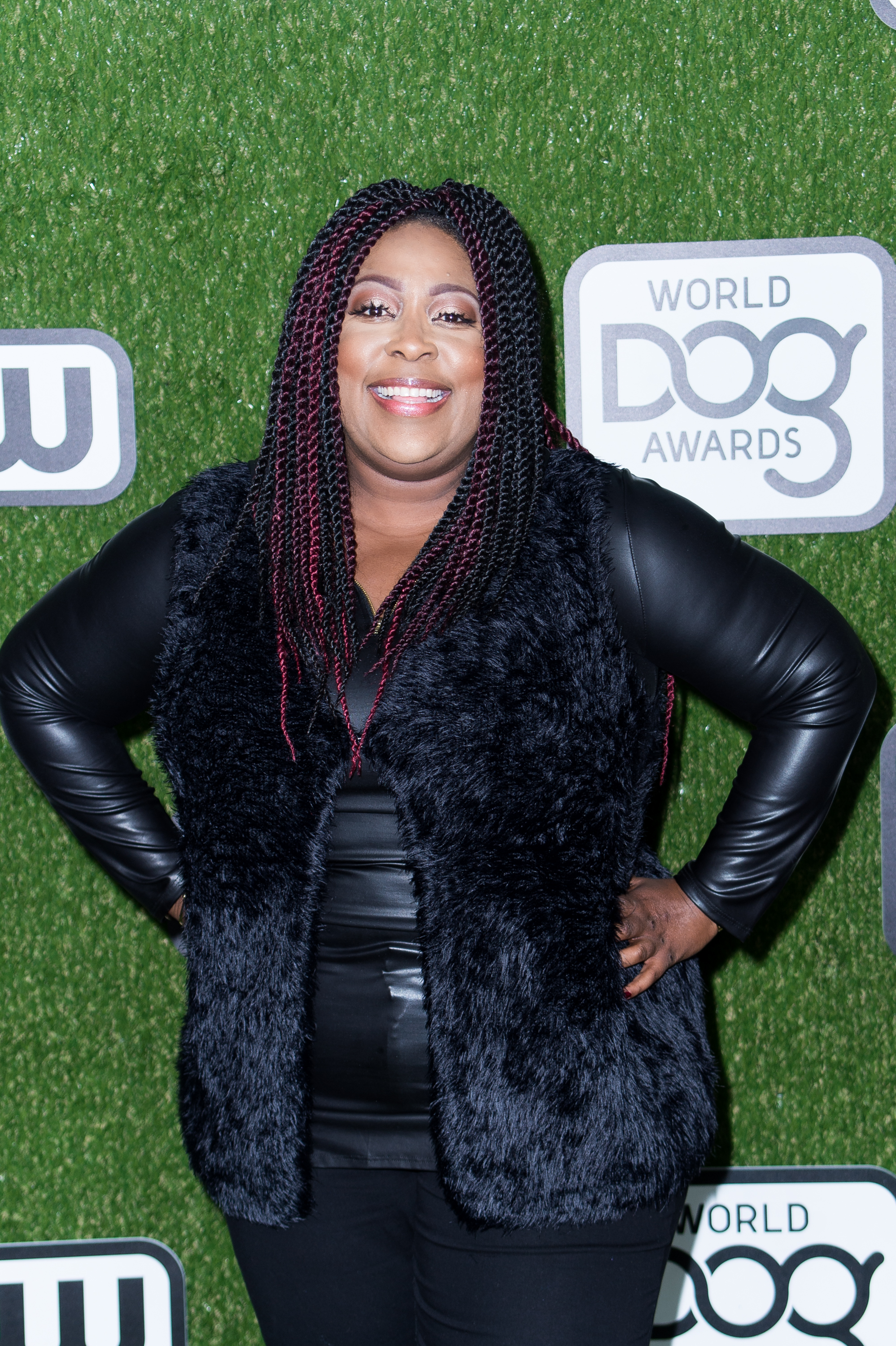 Loni Love attends the World Dog Awards at Barker Hangar on January 9, smiling brightly in an all-black outfit with a plush vest and braided hair accented with red highlights.