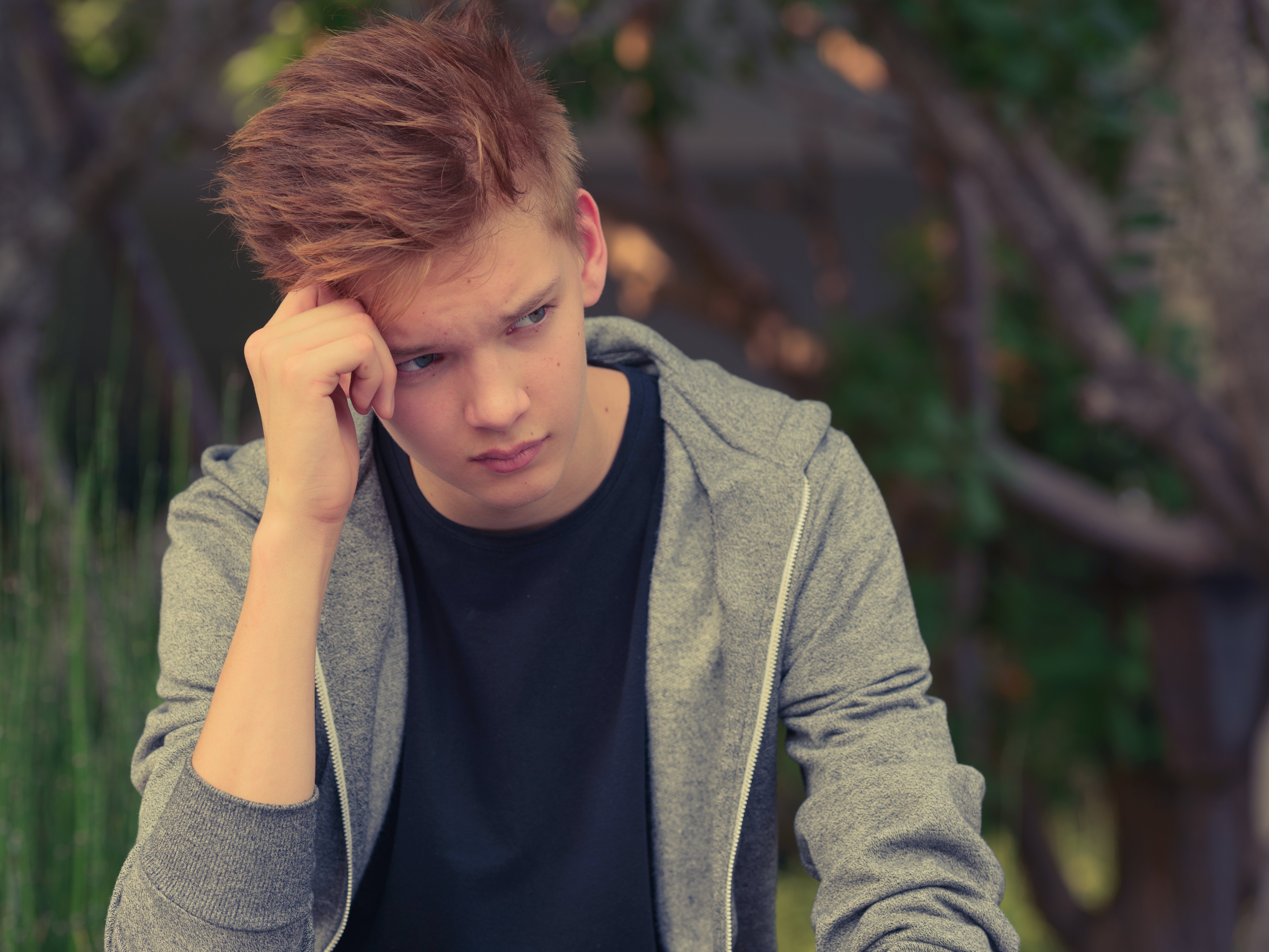 An upset teenager sitting with his hand against his head | Source: Shutterstock