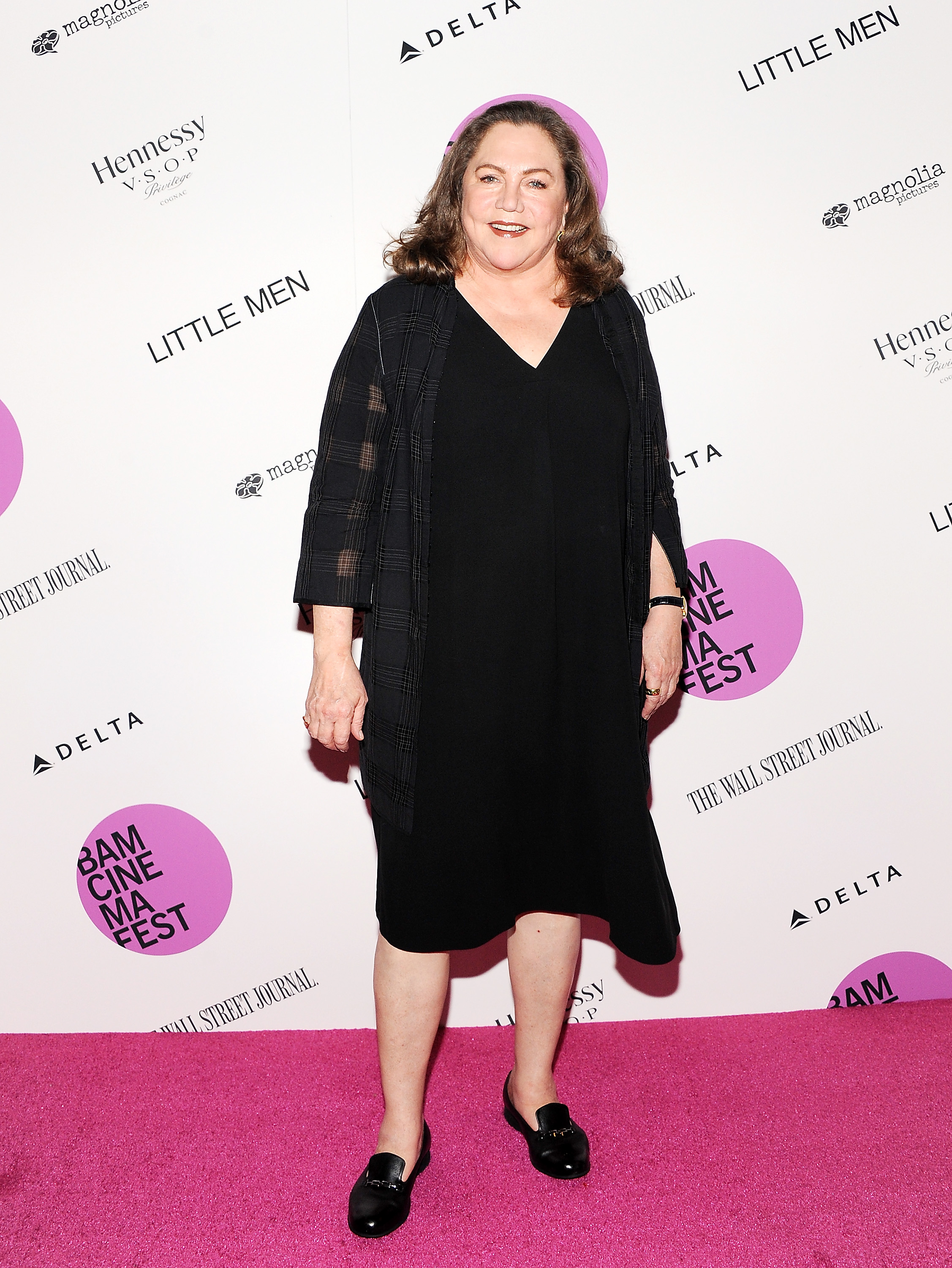 Kathleen Turner attends BAMcinemaFest 2016 Opening Night Premiere of "Little Men" in New York City. She looks chic in a simple black dress paired with a patterned jacket and black loafers, completing the look with a confident smile on the pink carpet.