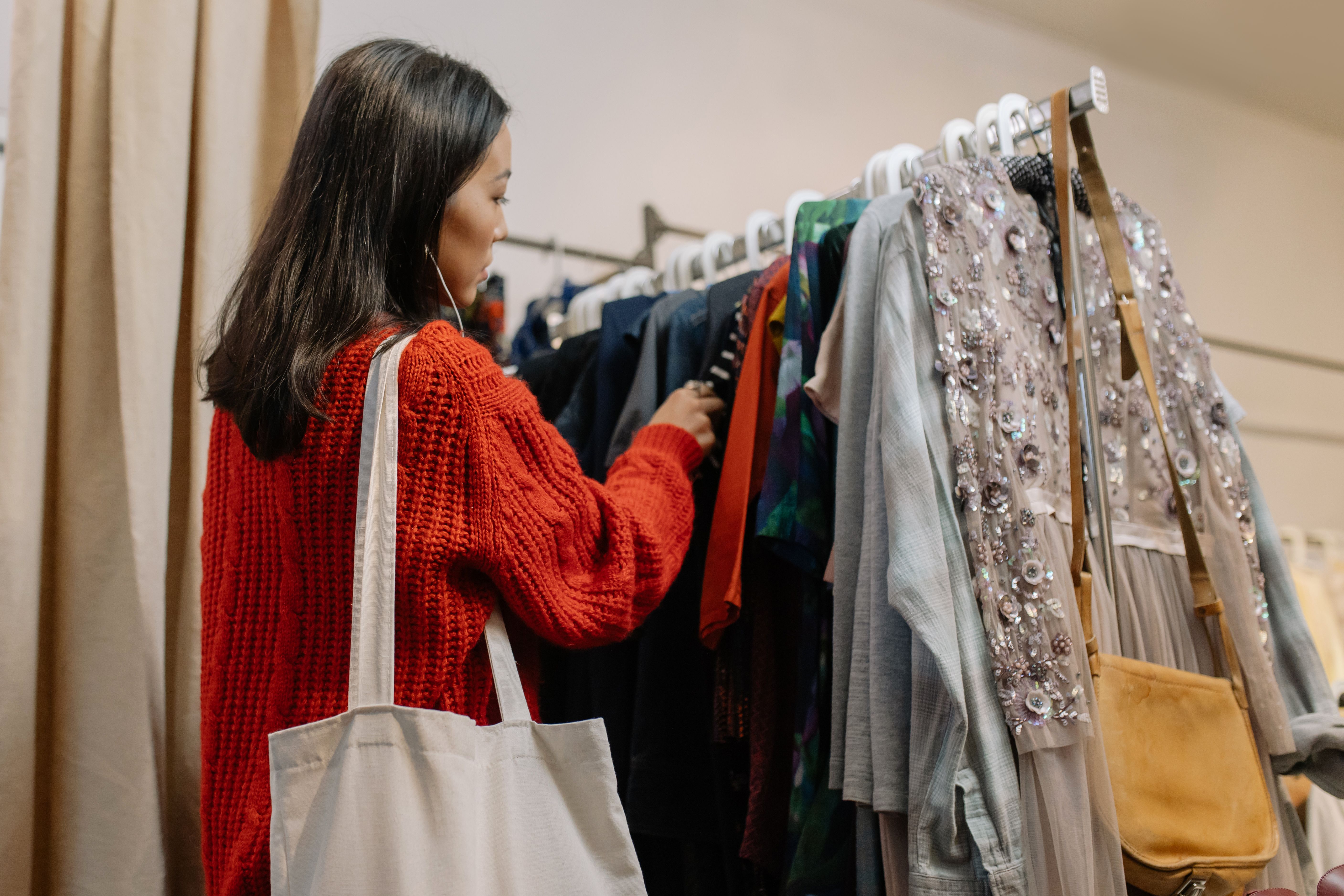 A woman in a red sweater browses a rack of clothing. | Source: Pexels