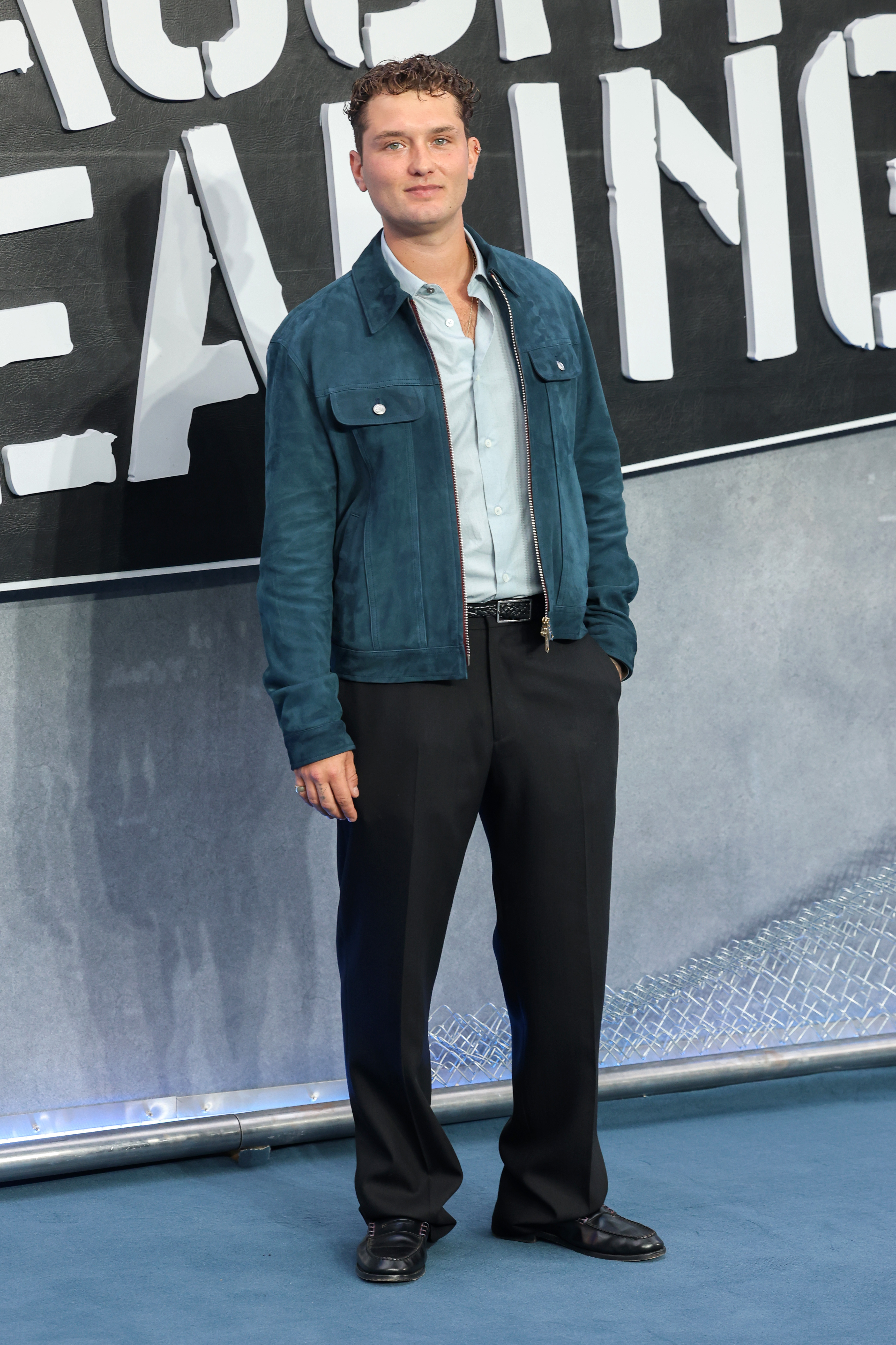 Raff Law at the "Caught Stealing" UK screening in London, August 2025 — the same curly dark hair as his father in his prime, wearing a teal suede jacket over a light blue shirt, his eyes and jaw unmistakably Law.