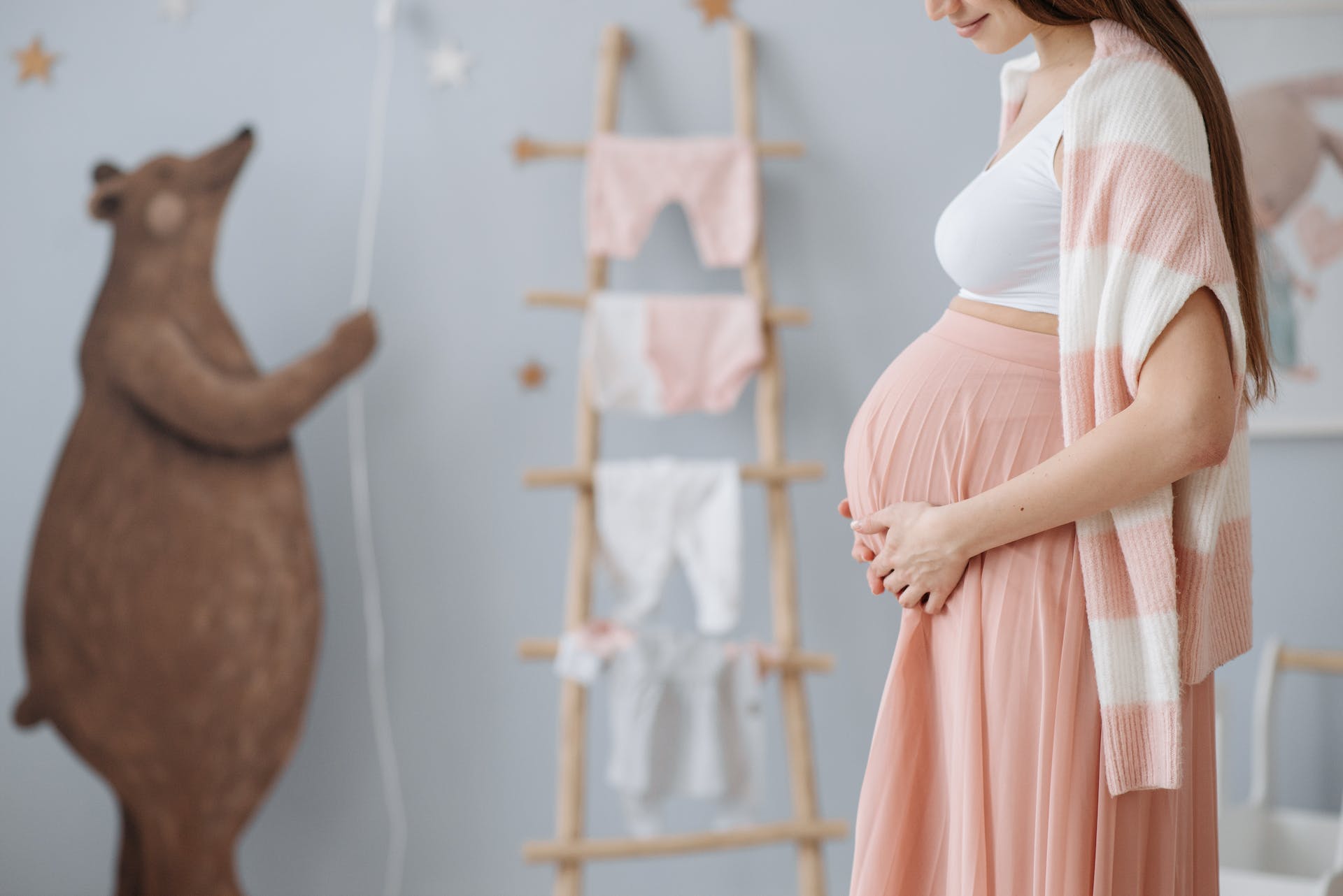 A pregnant woman holding her belly while in a baby's nursery | Source: Pexels