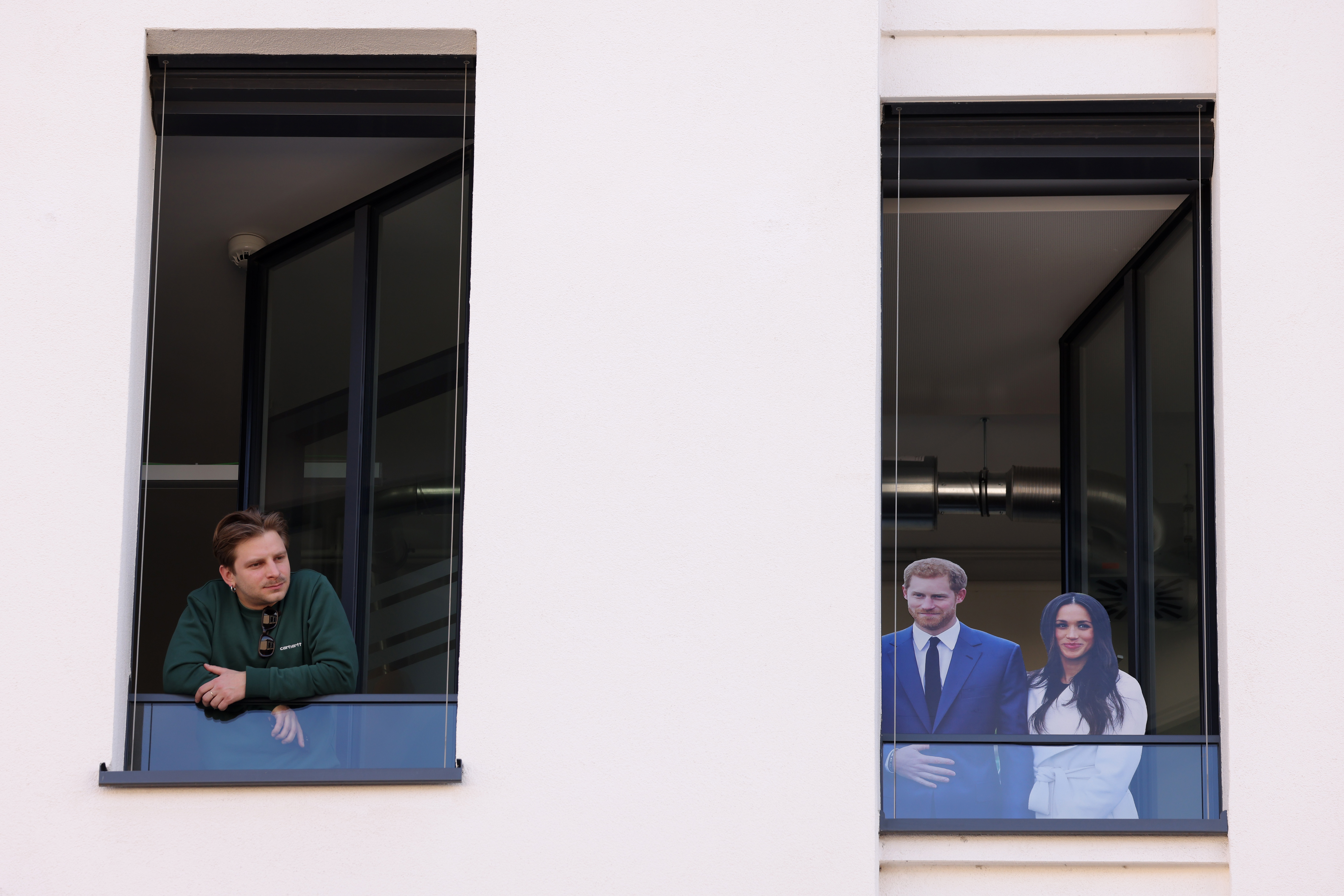 A spectator looks out of a window with a cut-out effigy of Prince Harry, Duke of Sussex and Meghan, Duchess of Sussex to see Camilla, Queen Consort in Komische Oper, on March 30, 2023 in Berlin, Germany. | Source: Getty Images