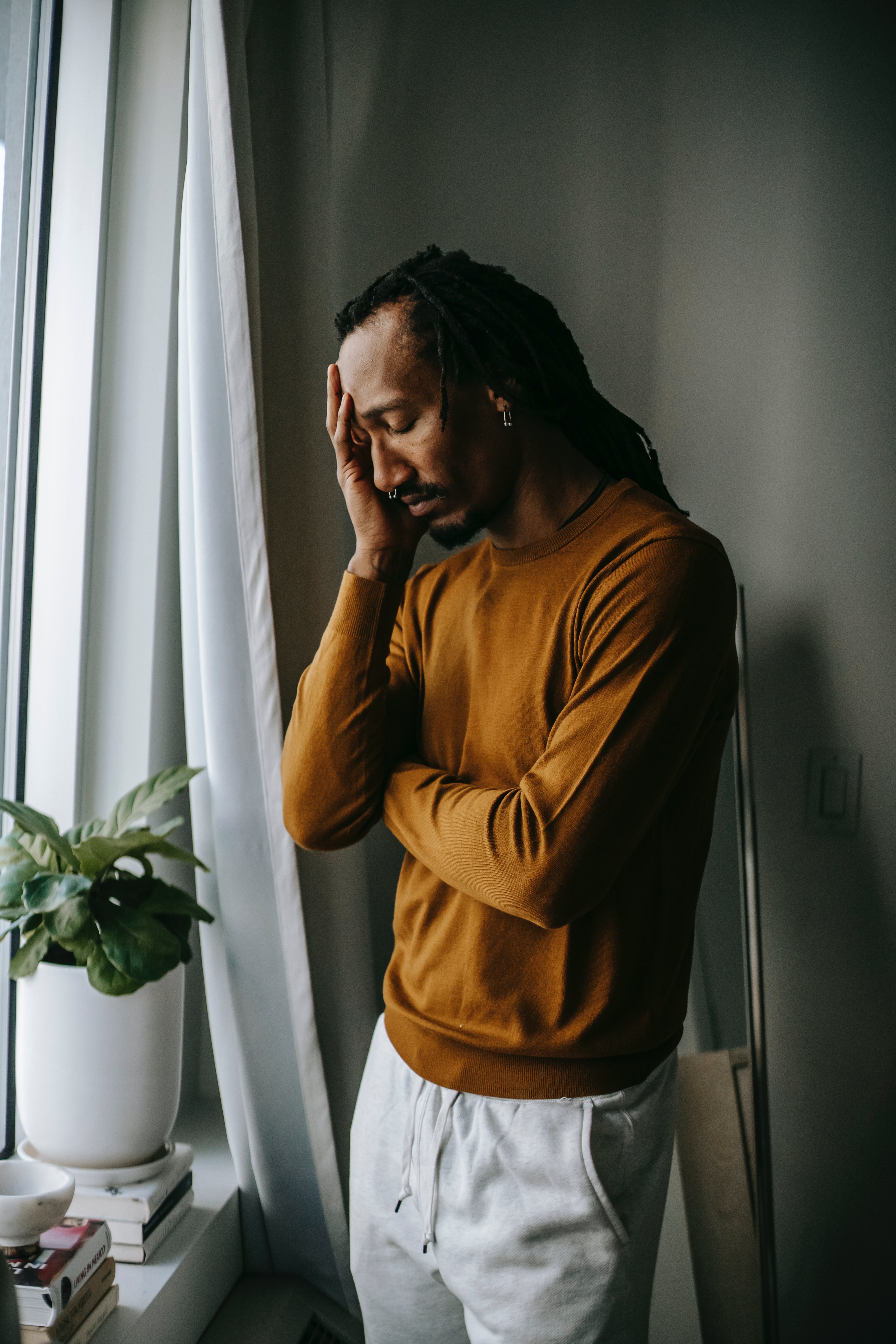 An upset man leaning against a wall covering his face with one hand | Source: Pexels