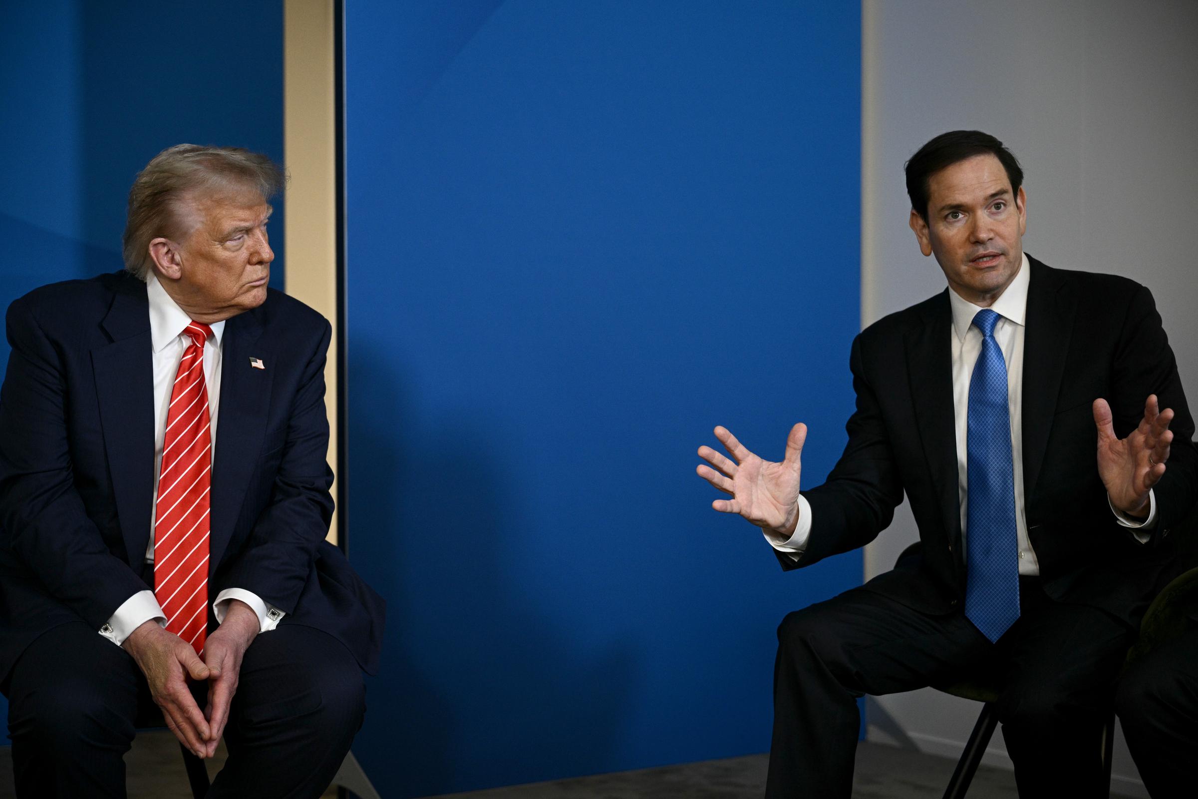 At the summit, Trump is seated beside U.S. Secretary of State Marco Rubio. He listens intently, his gaze fixed on Rubio as he speaks, capturing a focused moment of diplomacy and discussion amid the high-level talks.