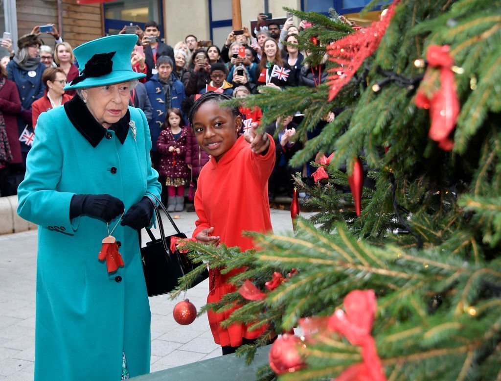 La reine Elizabeth II et Shylah Gordon, 8 ans, attachent une boule à un arbre de Noël lors de l'ouverture du centre Queen Elizabeth II à CORAM le 05 décembre 2018, à Londres, en Angleterre. | Source: Getty Images.