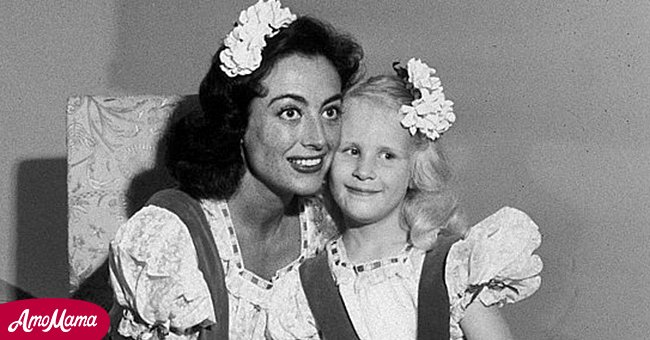 Joan Crawford sits and holds hands with her adopted daughter Christina at their home | Source: Amomama
